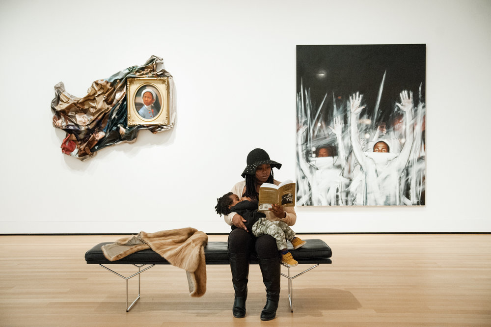 Amelia Sherwood, "being brave breastfeeding" in public, while reading in front of art by Titus Kaphar. Photo credit Rachel Liu