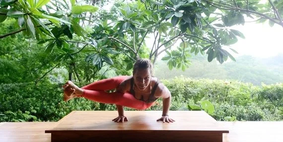 A woman practicing yoga in a treetop outdoor setting, balancing on a wooden surface while holding a plank position.