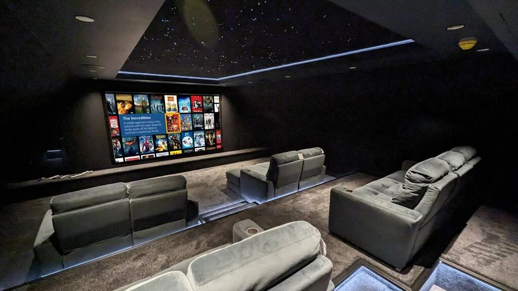 Home theater room with a large screen displaying a movie menu, plush gray couches, and a ceiling designed to resemble a starry night sky.