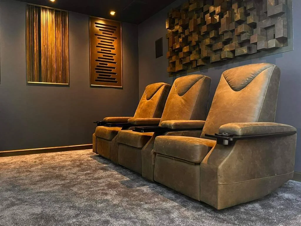 Three brown recliner chairs in a room with gray walls, acoustic panels, and artwork on the wall.