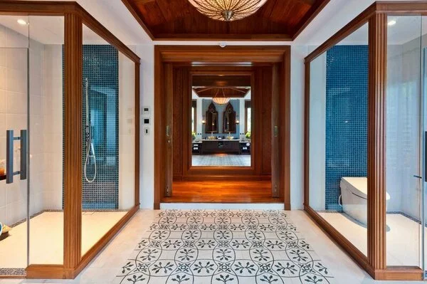 Hallway in a house with two glass-enclosed bathrooms with in-ceiling speakers on either side and a view into a living room at the end.