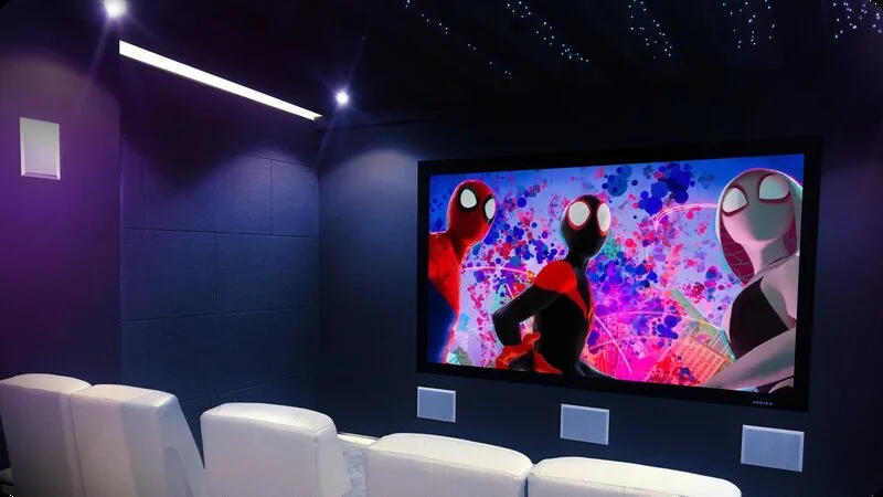 A home theater room with white leather chairs and a large screen showing Spider-Man comic-style artwork.
