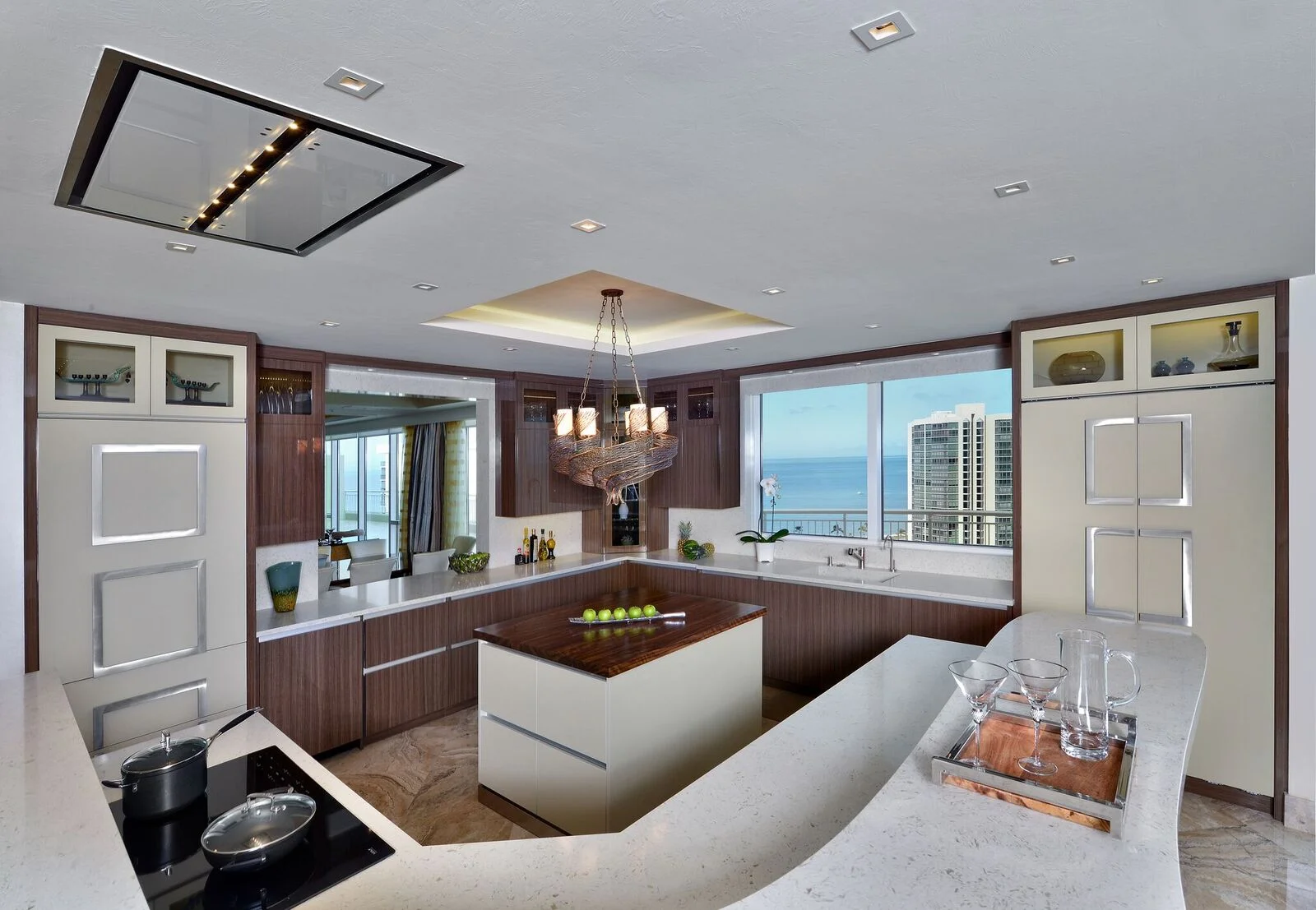 Following the client’s request to retain the original flooring, Naples Build worked within the footprint of the existing kitchen to bring to life this modern design. They first eliminated the upper cabinets, which opened up a spectacular view and brought in natural light. Then, with the addition of LED chip lights, they brightened the room without adding weight to the ceiling. The drawers are even lighted on the inside so they automatically turn on when opened. Custom handles on the appliance center, pantry, and refrigerator stylishly conceal the appliances. A wine cooler, icemaker, and microwave all hide behind new cabinet facing, and a custom hood with built-in lighting and glass panels is recessed into the ceiling to ensure that this kitchen looks clean and unobstructed. The free form quartz counter tops tastefully contrast the walnut island, diversifying the color palette and creating movement. Interesting and refined, this new kitchen achieves an aesthetic that vaults it into contemporary grandeur.