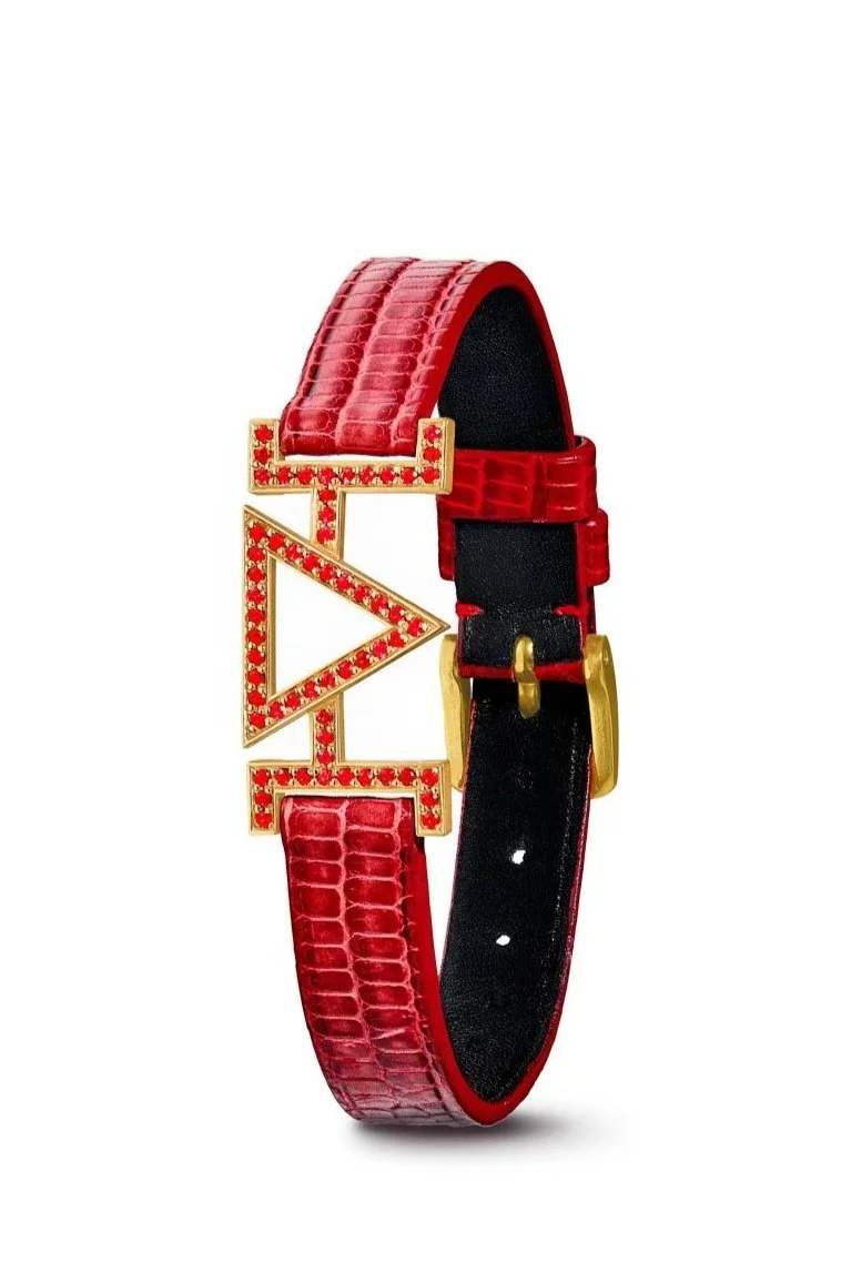 Bracelet en cuir rouge avec une boucle dorée et un pendentif orné de pierres rouges en forme de lettre et symbole.