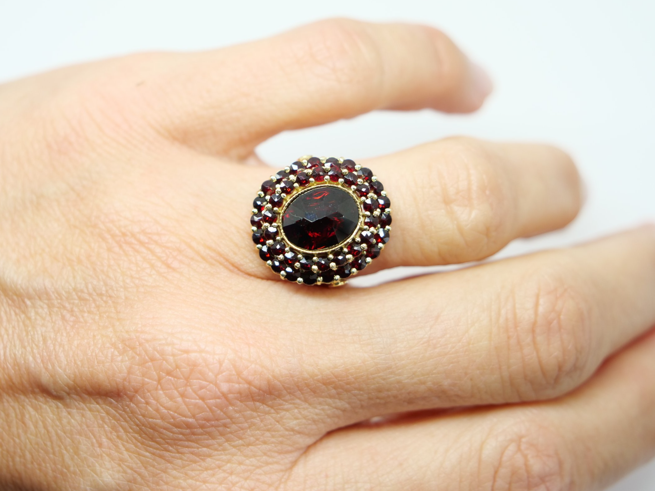 Beautiful 18ct gold garnet cocktail ring, set with an oval cut central garnet and surrounded by two rows of further garnets.