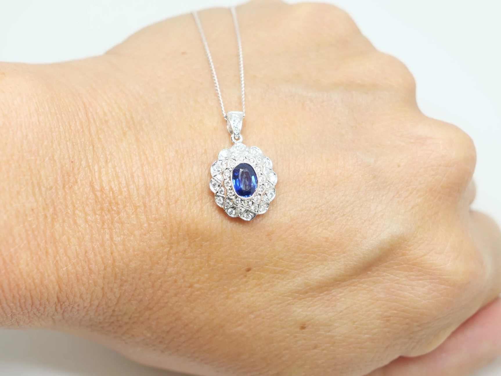 18ct white gold sapphire and diamond cluster pendant, oval blue sapphire in an ornate diamond surround, on an 18 inch chain