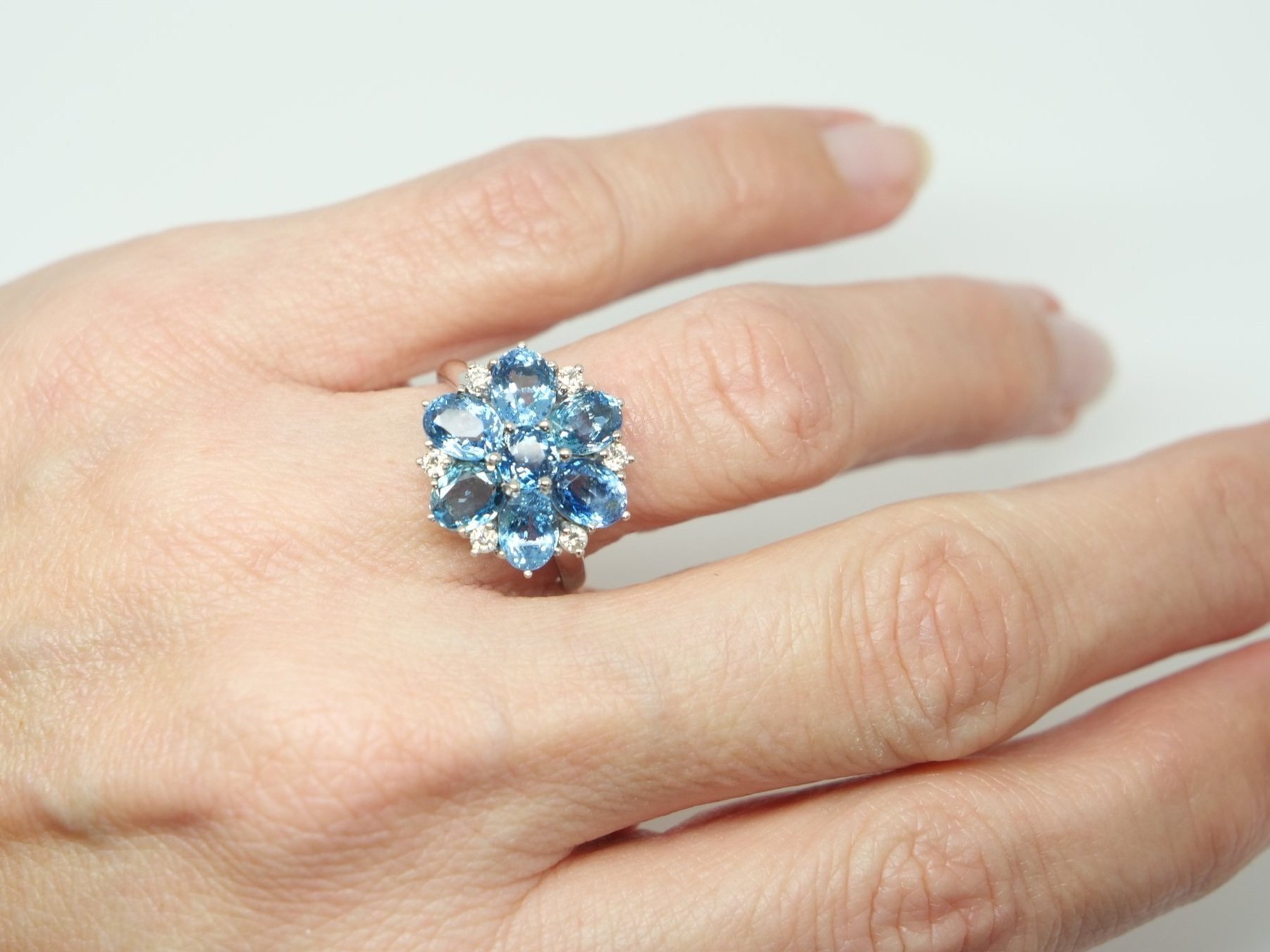 Very unusual 18ct gold aquamarine and diamond cocktail ring in a wonderful floral design. The ring is set with six oval cut mid blue aquamarines, with a round cut centre. Diamond accents.