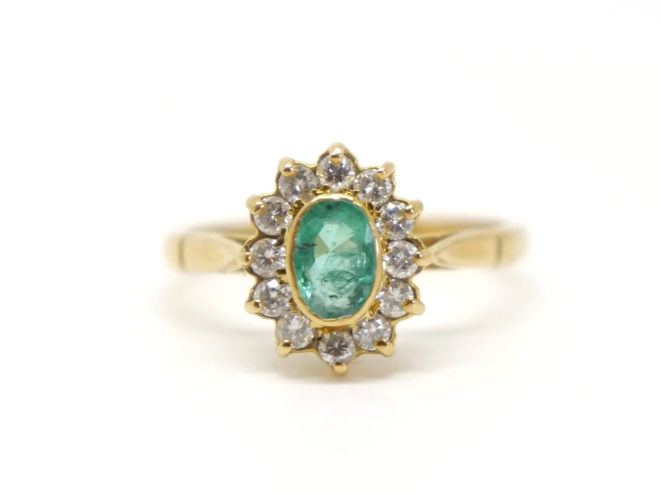 Classic vintage emerald and diamond cluster ring, set with a central oval cut emerald and surrounded by diamonds. All set in 18ct gold.