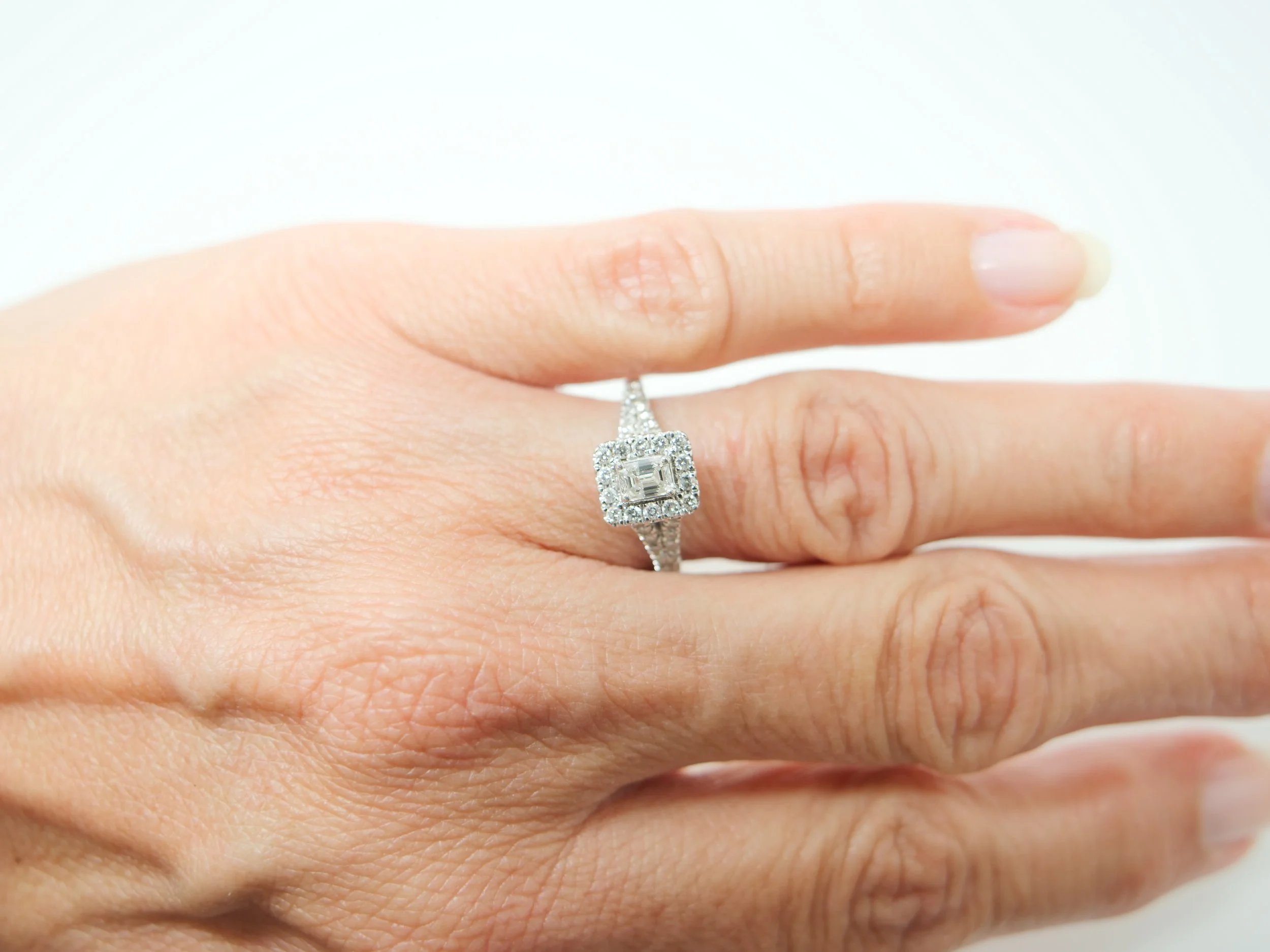 platinum diamond cluster ring set with an emerald-cut diamond at the centre, surrounded by a rectangular pavé-set halo of round brilliant-cut diamonds
