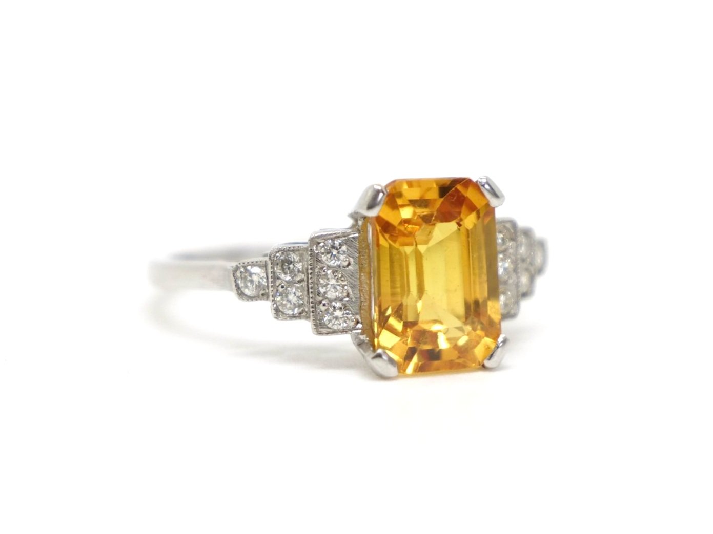 Art Deco style platinum yellow sapphire and diamond ring, set with an emerald cut yellow sapphire of approximately 2.5ct. Diamonds set into step design to each shoulder.