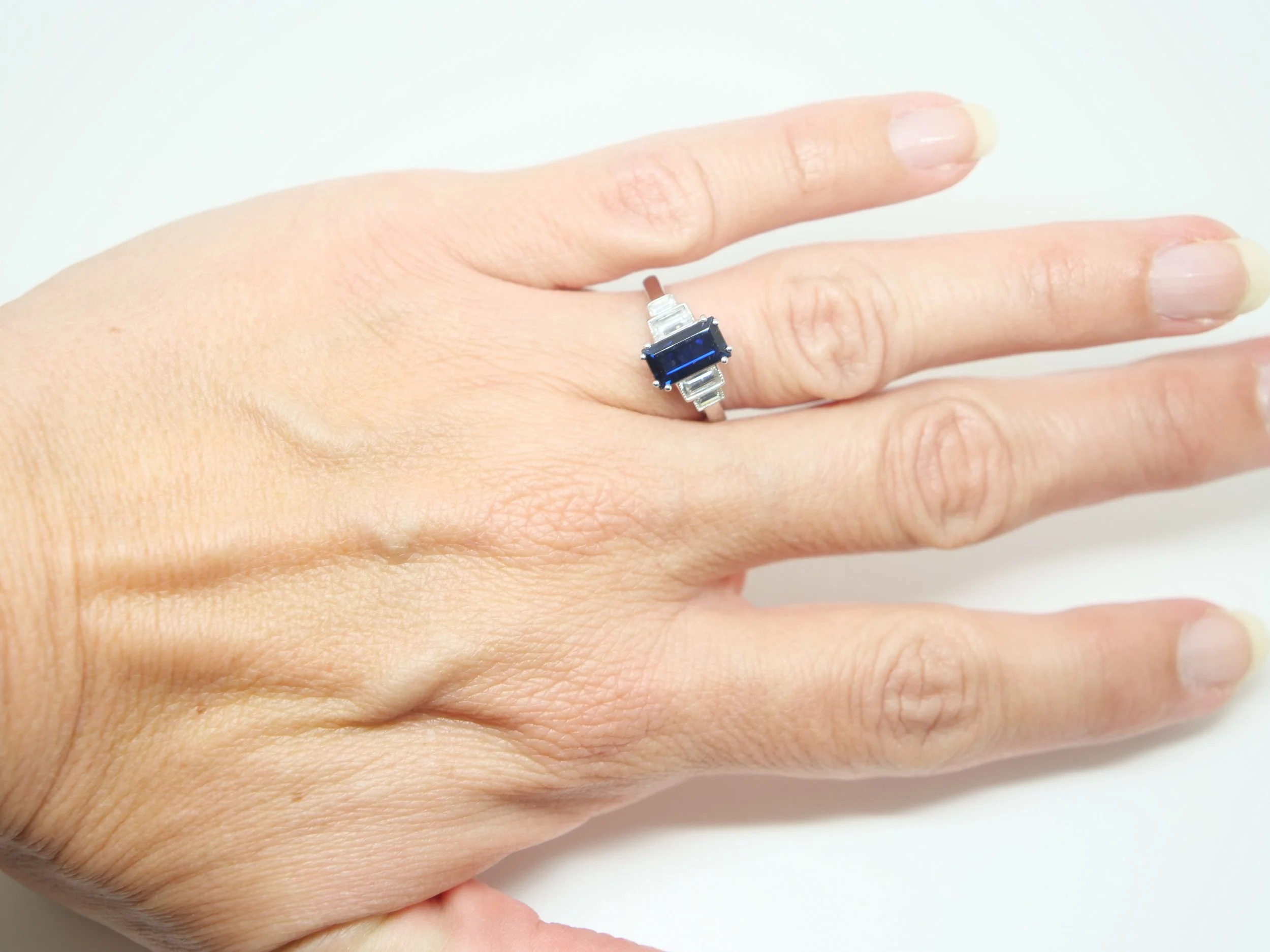 Super quality ring in platinum, set with a 1.5ct emerald cut sapphire, with two baguette cut diamonds to each side. Milgrain edging around diamonds.