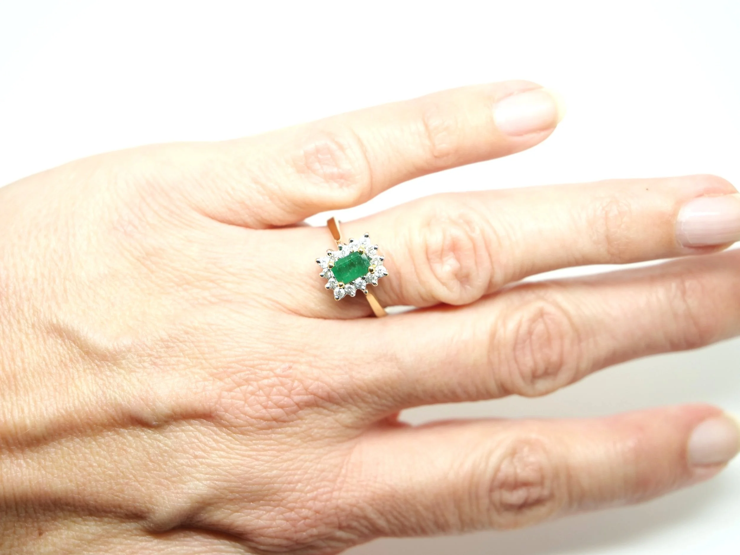 Lovely vintage emerald and diamond ring, set with a central emerald cut natural emerald and surrounded by small diamonds. All set in 18ct gold.