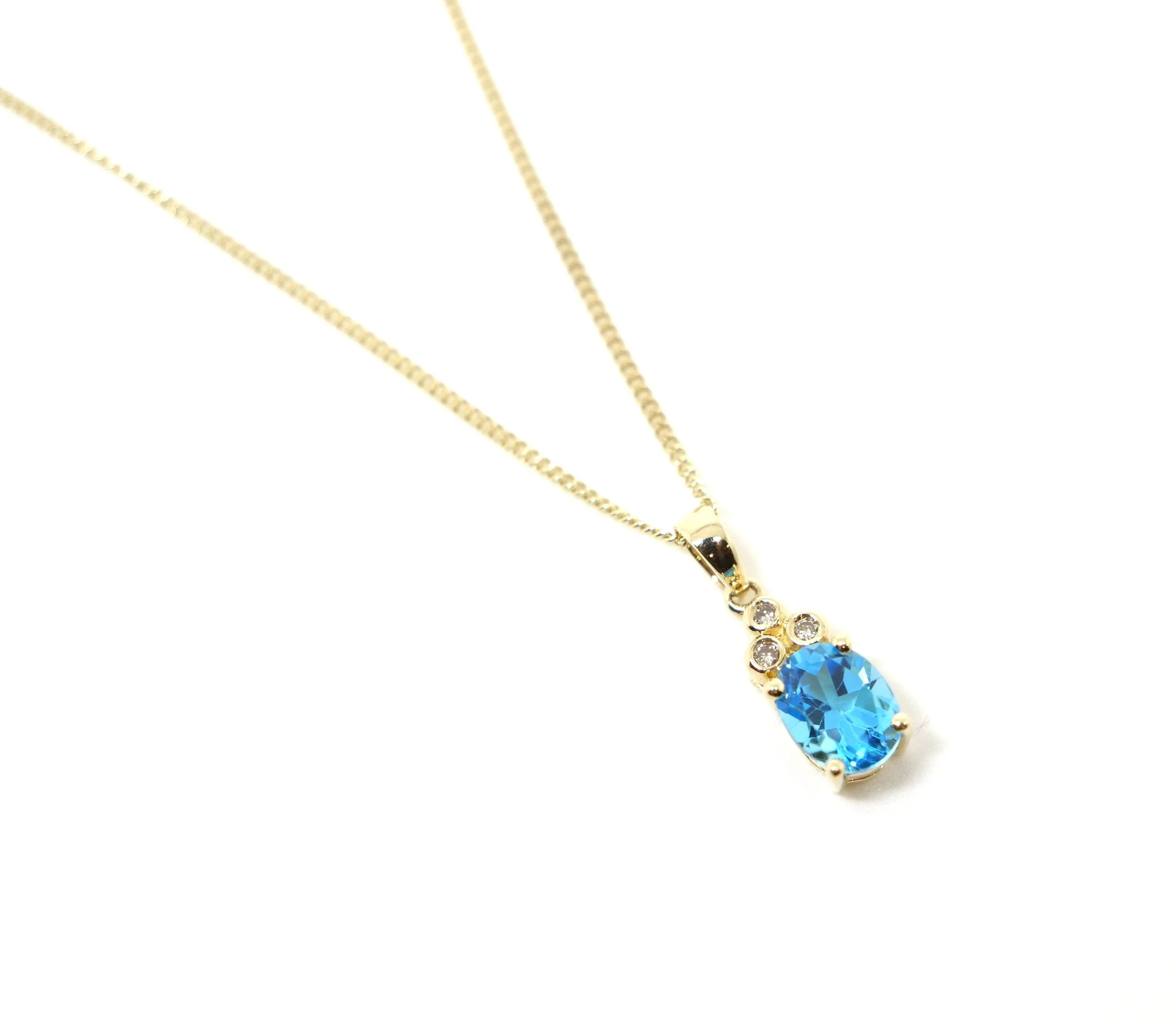 Very pretty 14ct gold pendant, with an oval cut blue topaz in an eye catching vivid blue, with three small rub over set diamonds above. With 9ct gold chain.