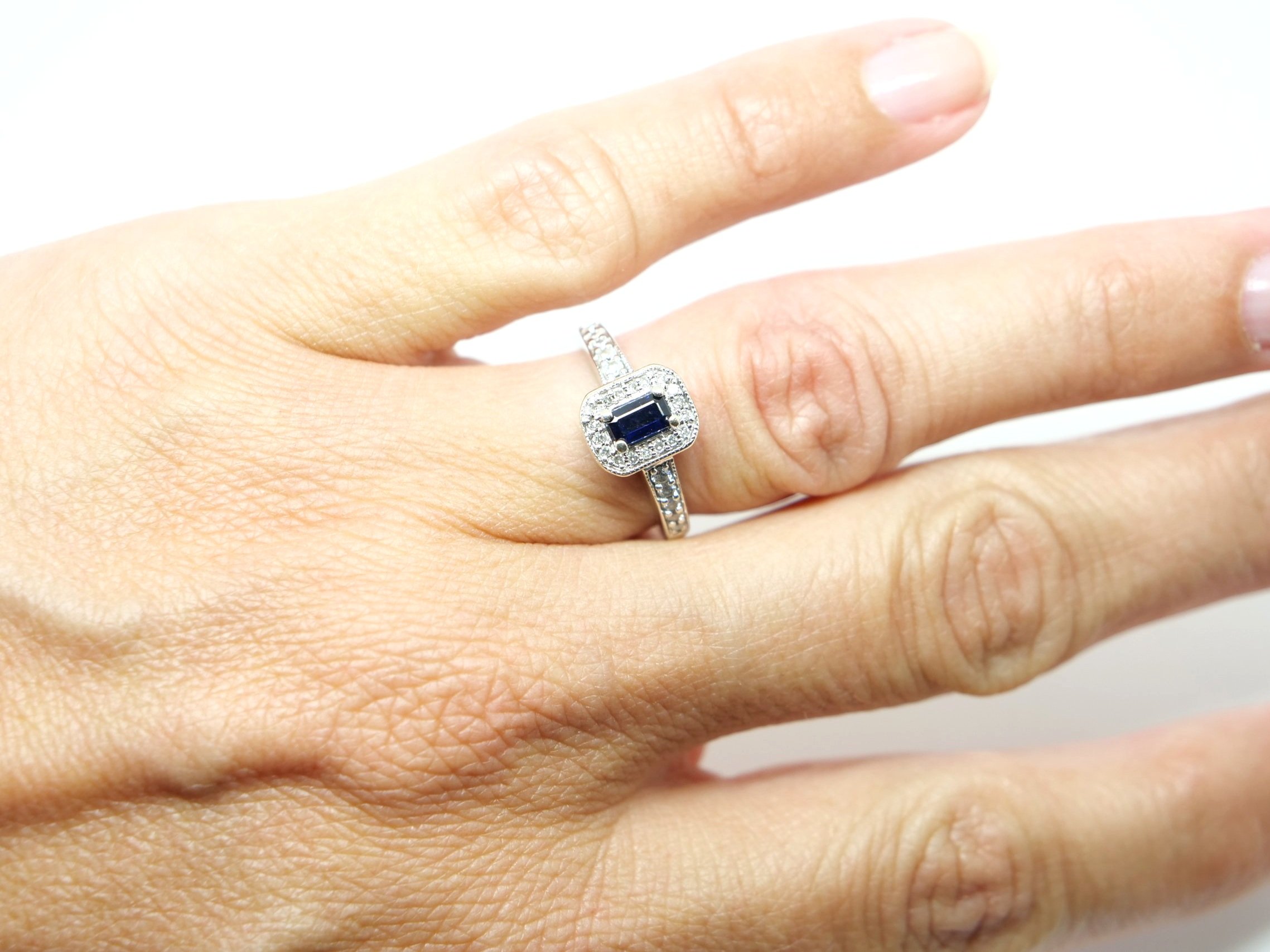 Contemporary 9ct white gold sapphire and diamond ring, in classic style, set with an emerald cut sapphire and surrounded by diamonds. Further diamonds to each shoulder.