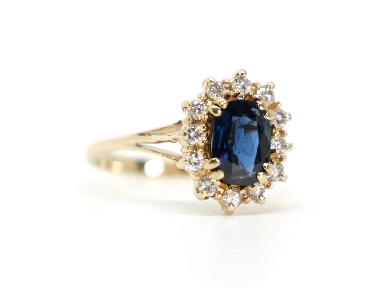 Classic sapphire and diamond cluster ring in 14ct gold, set with an oval cut sapphire of approximately 1.5ct and surrounded by diamonds.