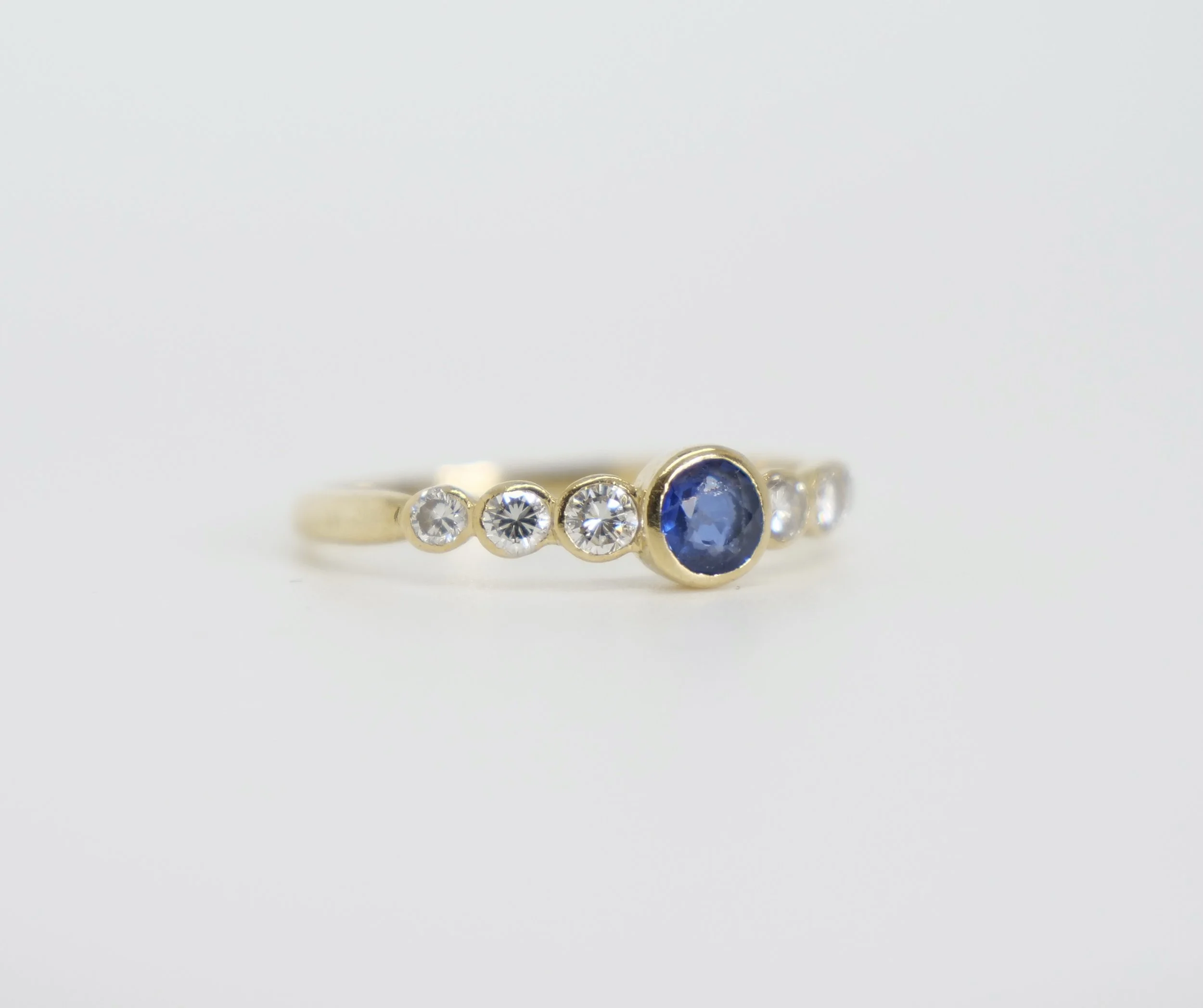 Unusual vintage 18ct gold sapphire and diamond ring, set with a central bezel set sapphire, with three diamonds to each shoulder.