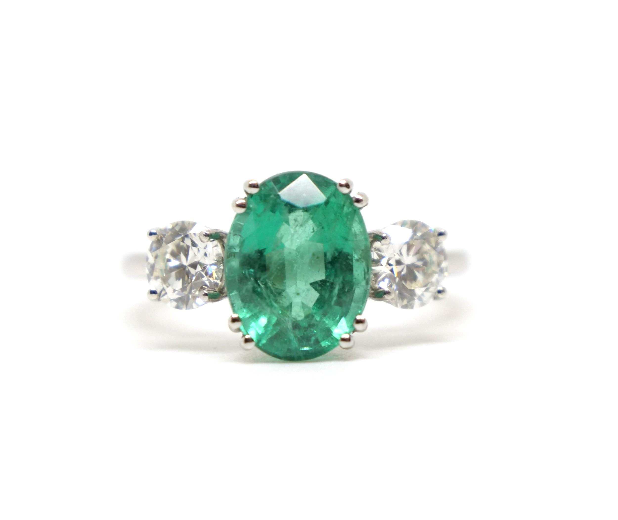 Beautiful platinum emerald and diamond three stone ring, set with a central oval cut natural emerald of approximately 3cts, with a brilliant cut diamond to each shoulder.