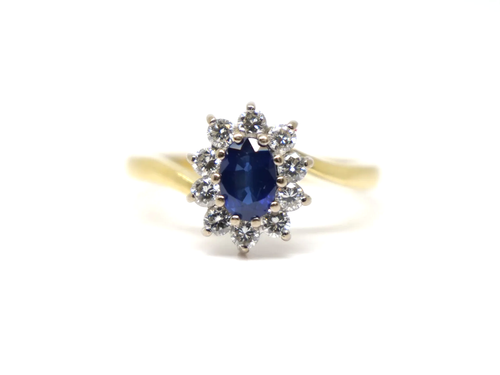 An 18ct gold sapphire and diamond cluster ring from 1998, set with an oval cut sapphire of approximately 0.6 carats at the centre, surrounded by ten round brilliant cut diamonds of 0.4 carats