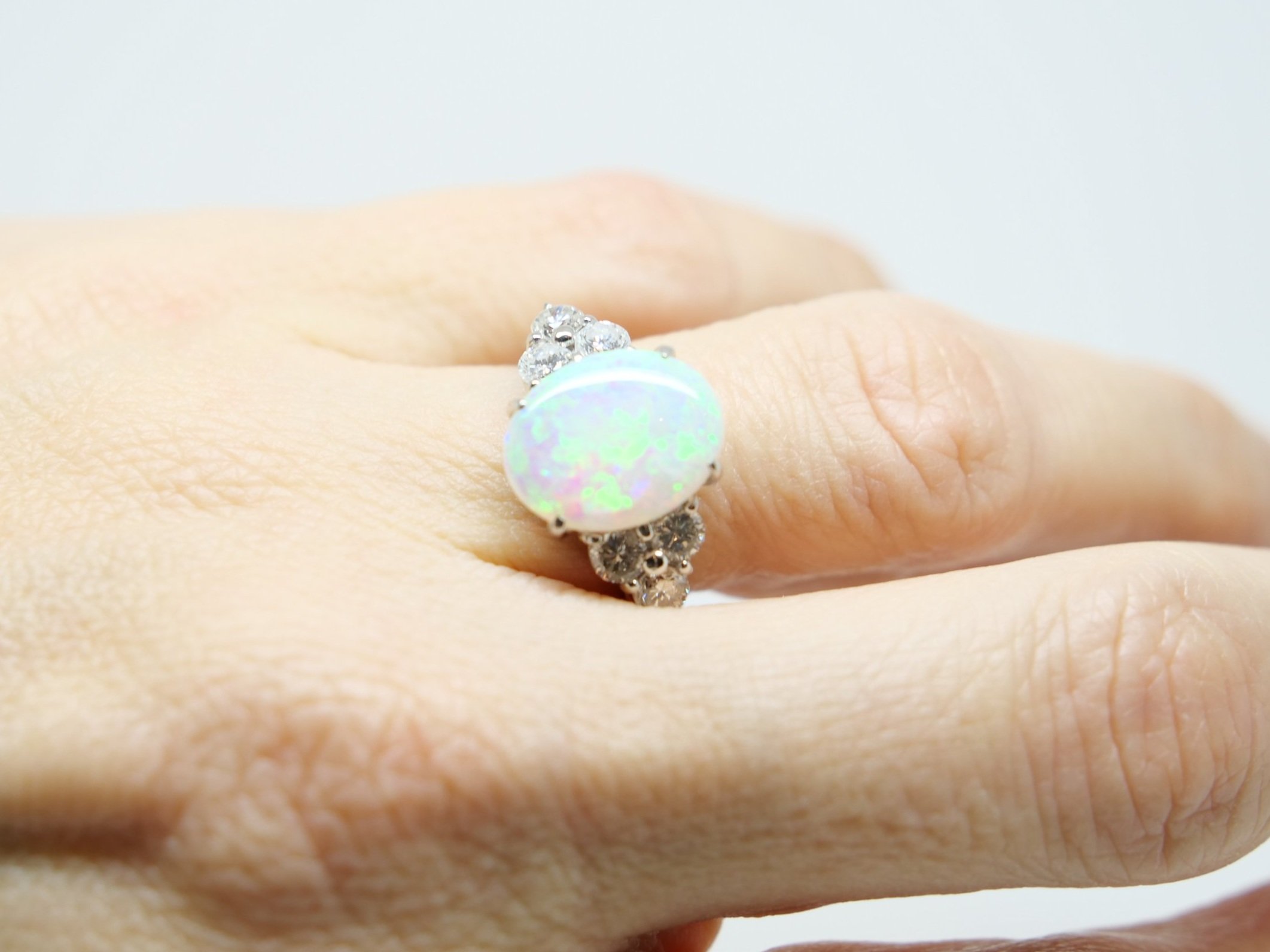 Stunning platinum opal and diamond ring, set with a beautiful opal with pink and green hues, with three diamonds to each side.