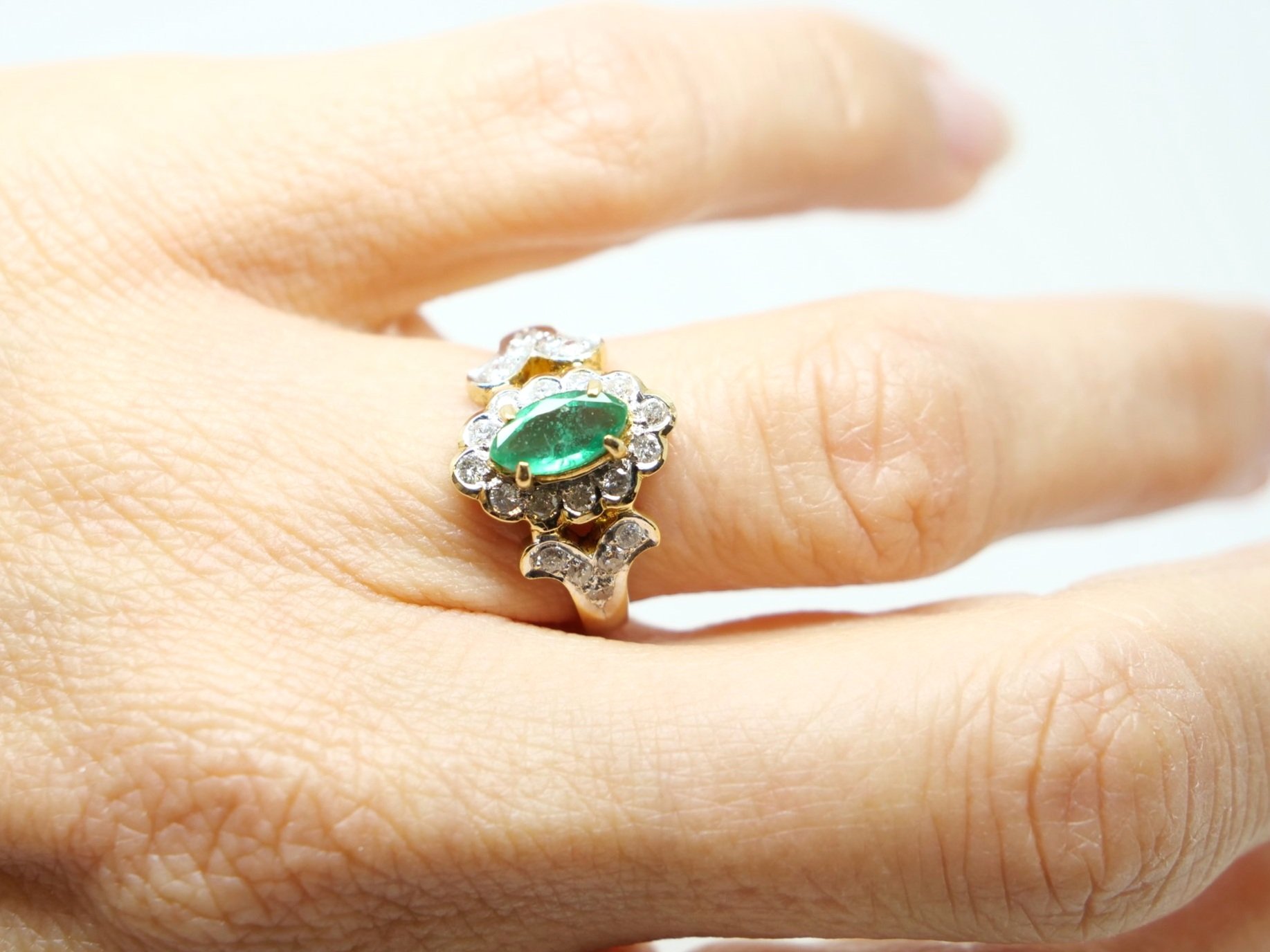 Very unusual 18ct gold emerald and diamond ring, set with a marquise cut central emerald and surrounded by diamonds. Further diamonds to each shoulder.