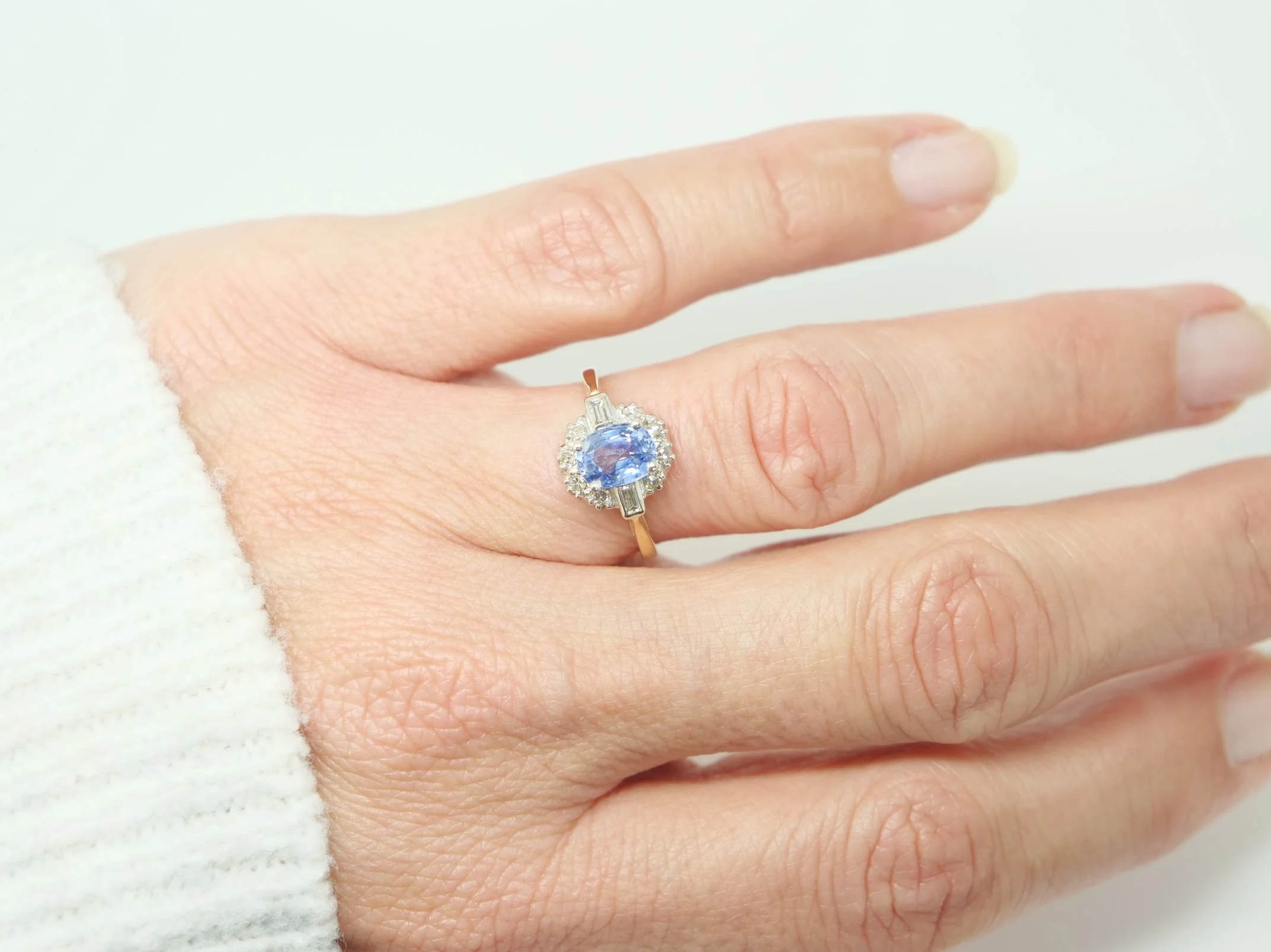 Stunning 18ct gold sapphire and diamond ring, set with an oval light blue sapphire and surrounded by diamonds, with a baguette diamond to each shoulder.