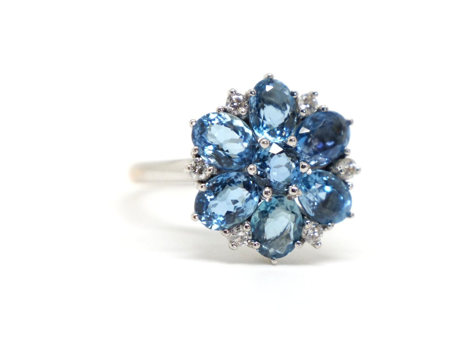 Very unusual 18ct gold aquamarine and diamond cocktail ring in a wonderful floral design. The ring is set with six oval cut mid blue aquamarines, with a round cut centre. Diamond accents.
