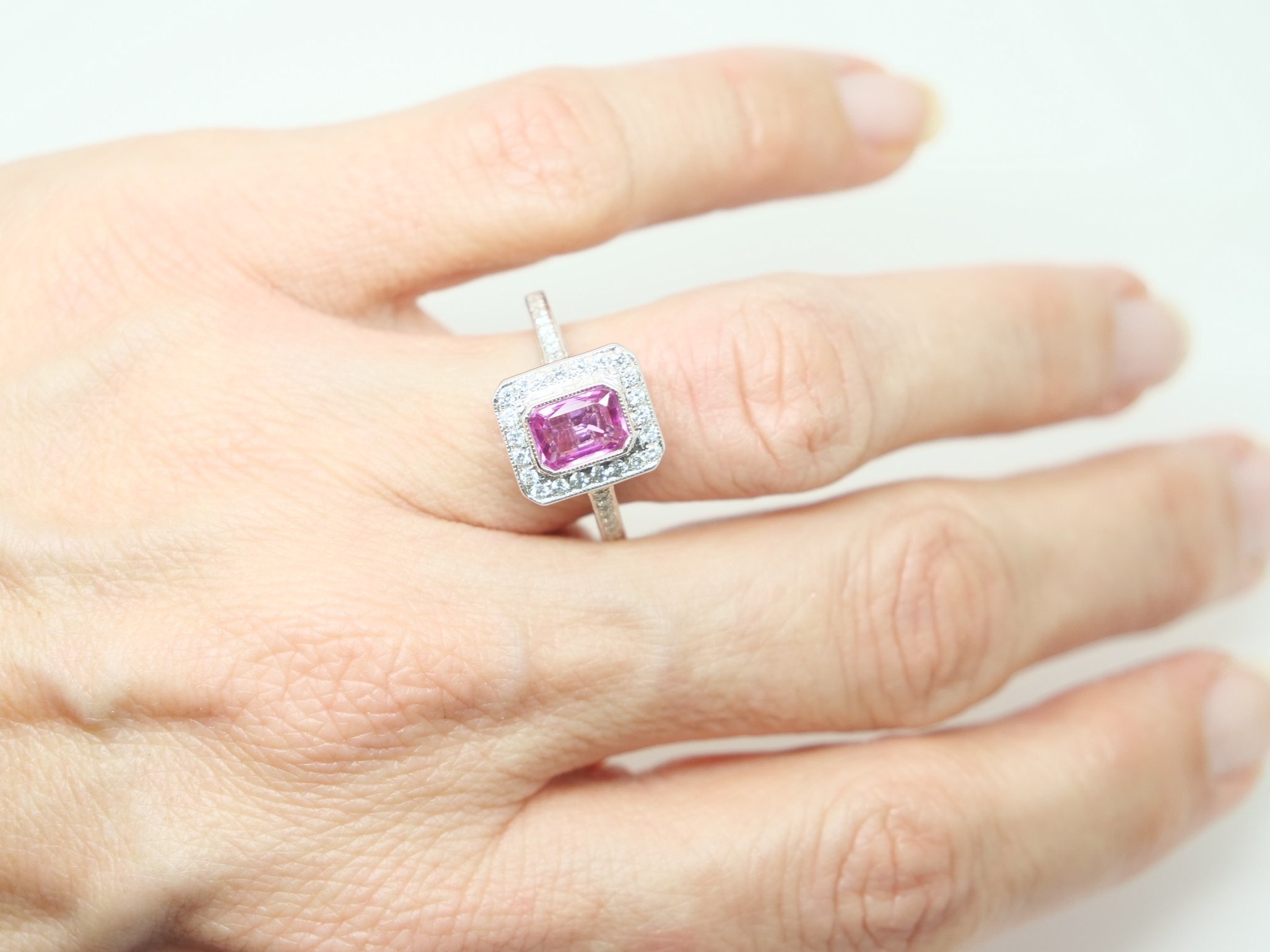 Lovely 18ct gold pink sapphire and diamond ring, set with a centre emerald cut pink sapphire of approximately 1.15cts, surrounded by diamonds. Further diamonds to each shoulder.