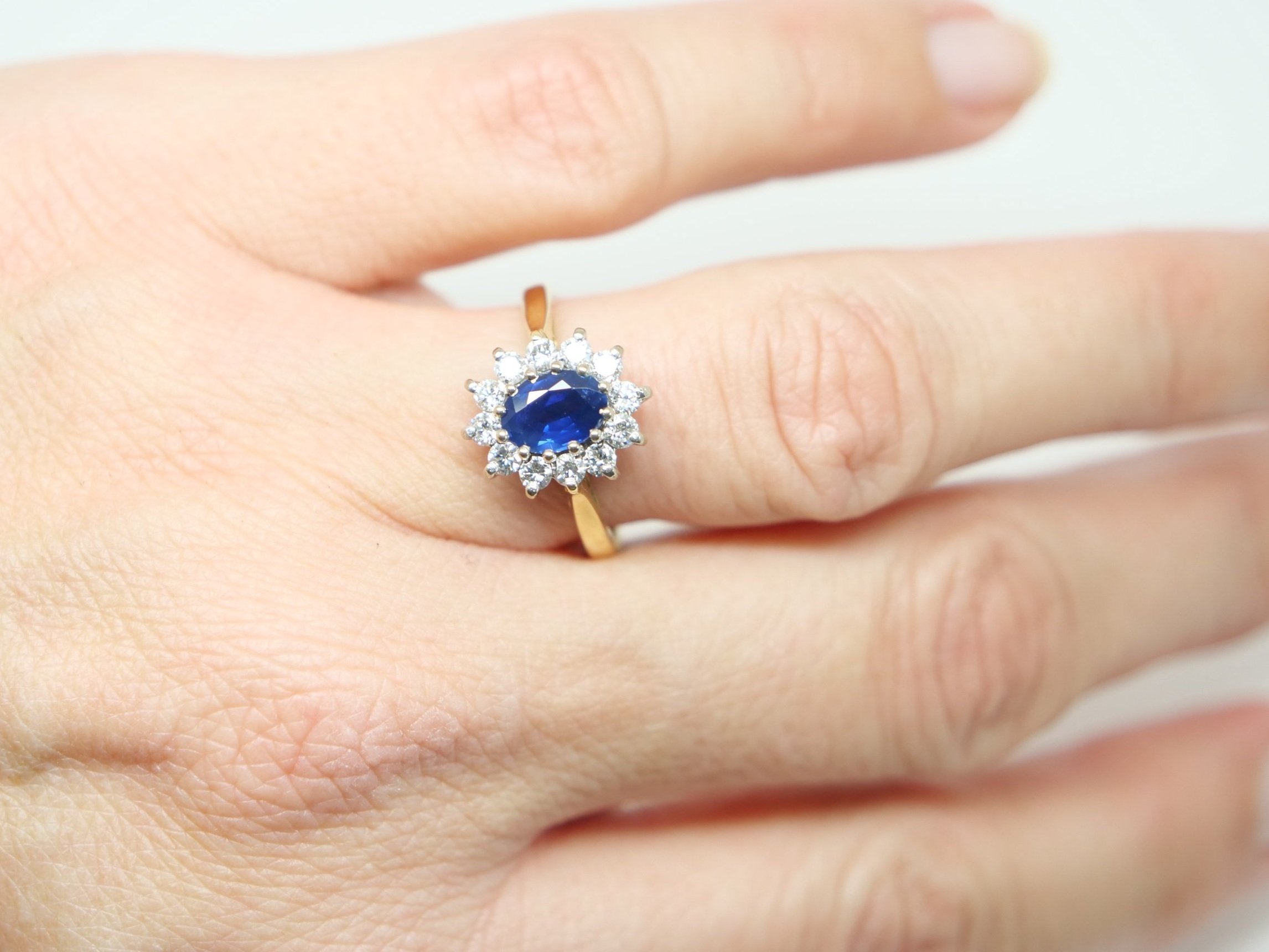 Classic 18ct sapphire and diamond cluster ring, set with an oval cut 1ct sapphire and surrounded by brilliant cut diamonds.