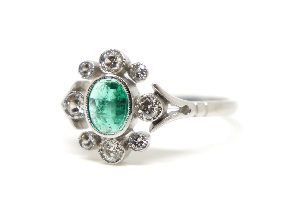 Super vintage style platinum oval cut emerald and diamond ring, set with a 0.6ct oval cut emerald with eight diamonds in this pretty design.