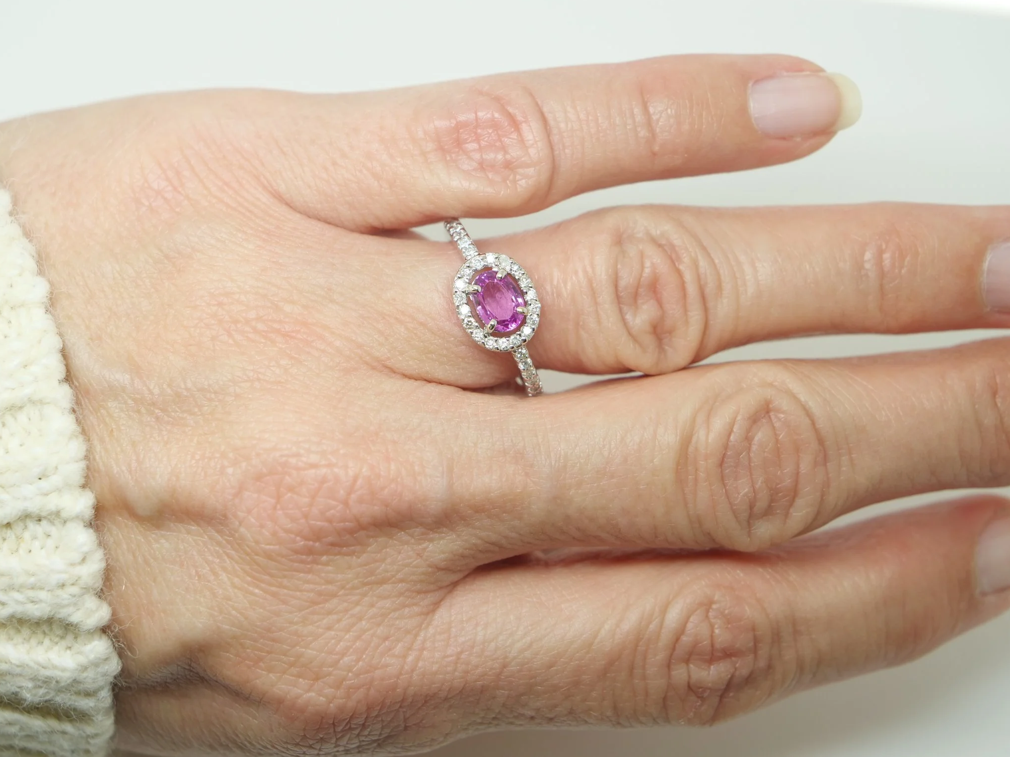 Very sparkly contemporary 18ct gold pink sapphire and diamond ring, set with an oval cut east-west pink sapphire, with a diamond halo. Further diamonds to the shoulders.