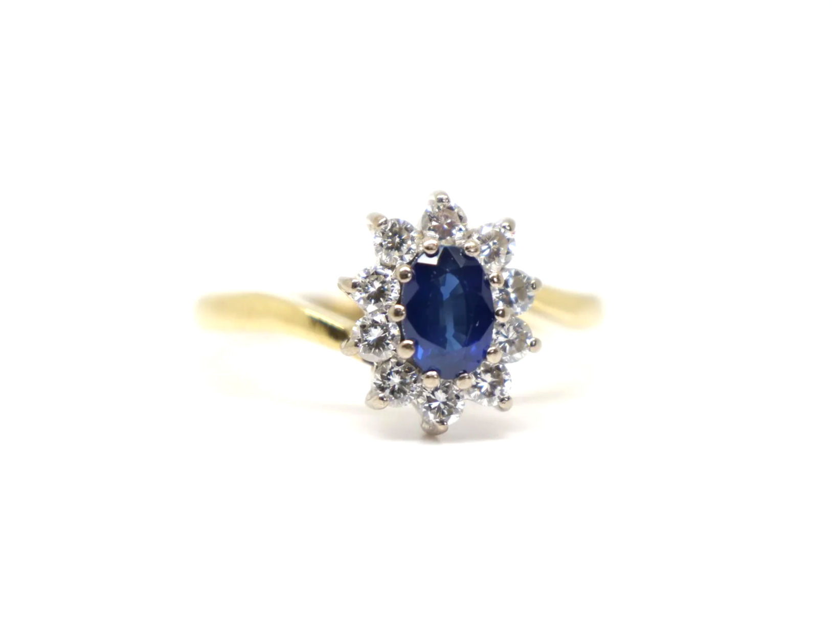 An 18ct gold sapphire and diamond cluster ring from 1998, set with an oval cut sapphire of approximately 0.6 carats at the centre, surrounded by ten round brilliant cut diamonds of 0.4 carats