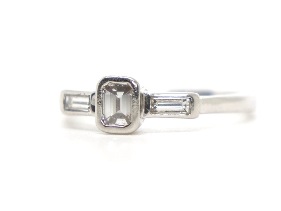 Unusual platinum diamond ring, set with a central emerald cut diamond, with a baguette cut diamond to each shoulder. Total diamond weight 0.5ct.