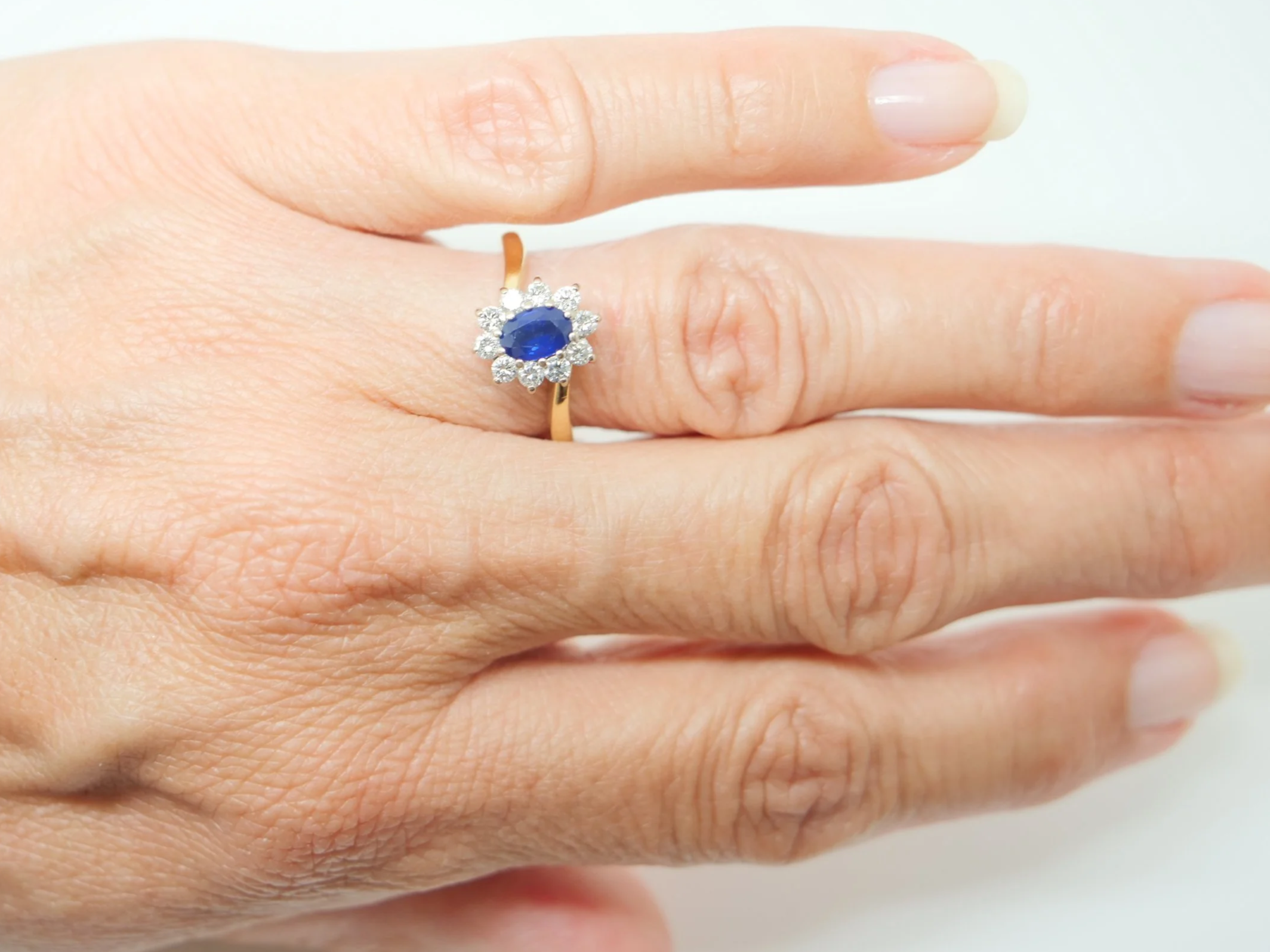 An 18ct gold sapphire and diamond cluster ring from 1998, set with an oval cut sapphire of approximately 0.6 carats at the centre, surrounded by ten round brilliant cut diamonds of 0.4 carats