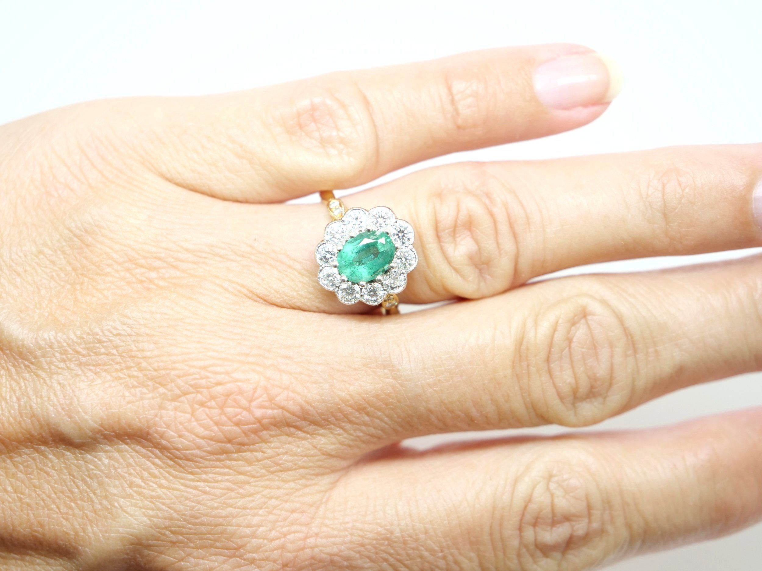 18ct gold vintage emerald and diamond ring, set with a large oval cut natural emerald of approximately 1.1cts. Brilliant cut diamonds set around the emerald, with small diamonds to each shoulder.