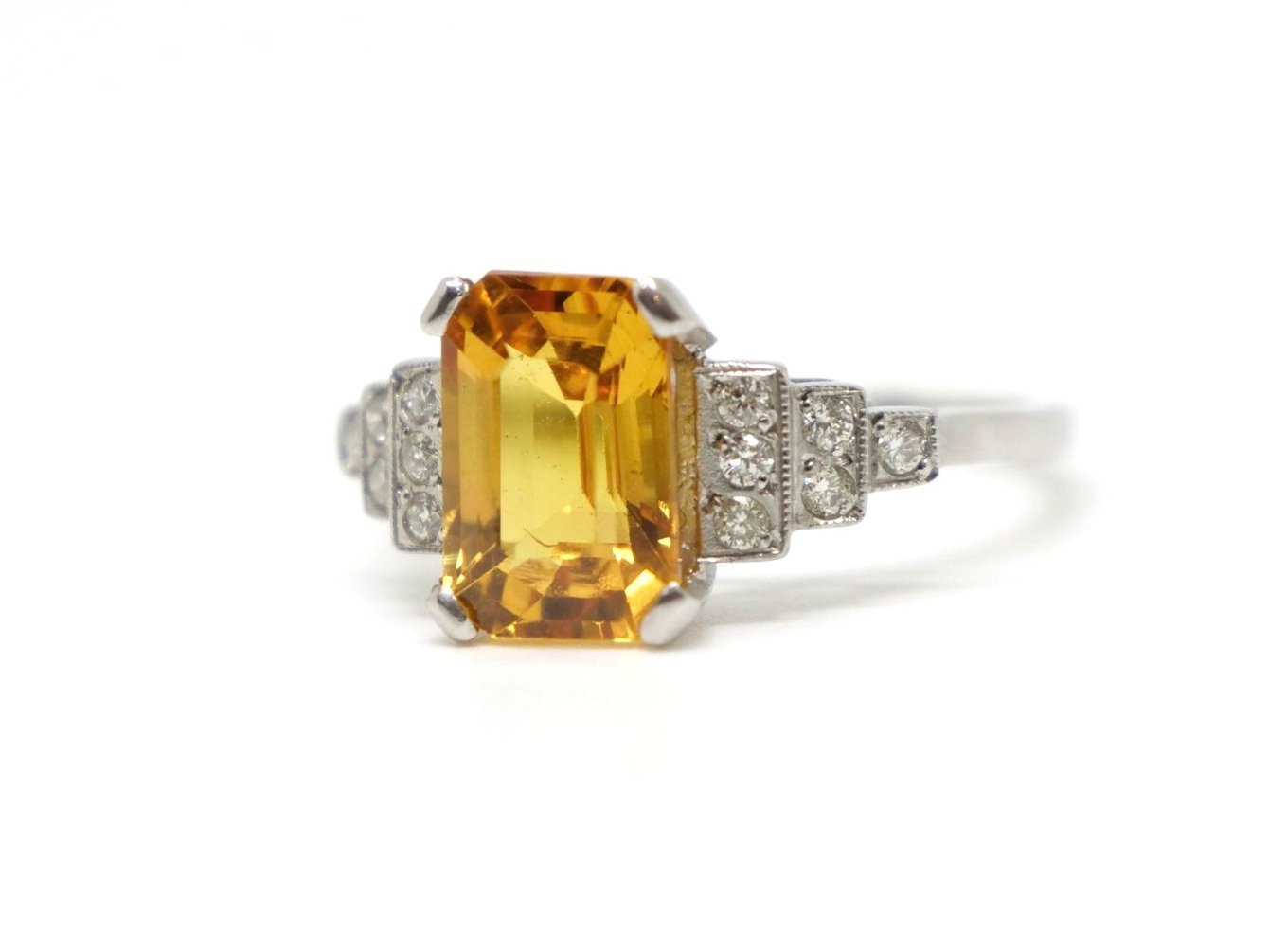 Art Deco style platinum yellow sapphire and diamond ring, set with an emerald cut yellow sapphire of approximately 2.5ct. Diamonds set into step design to each shoulder.