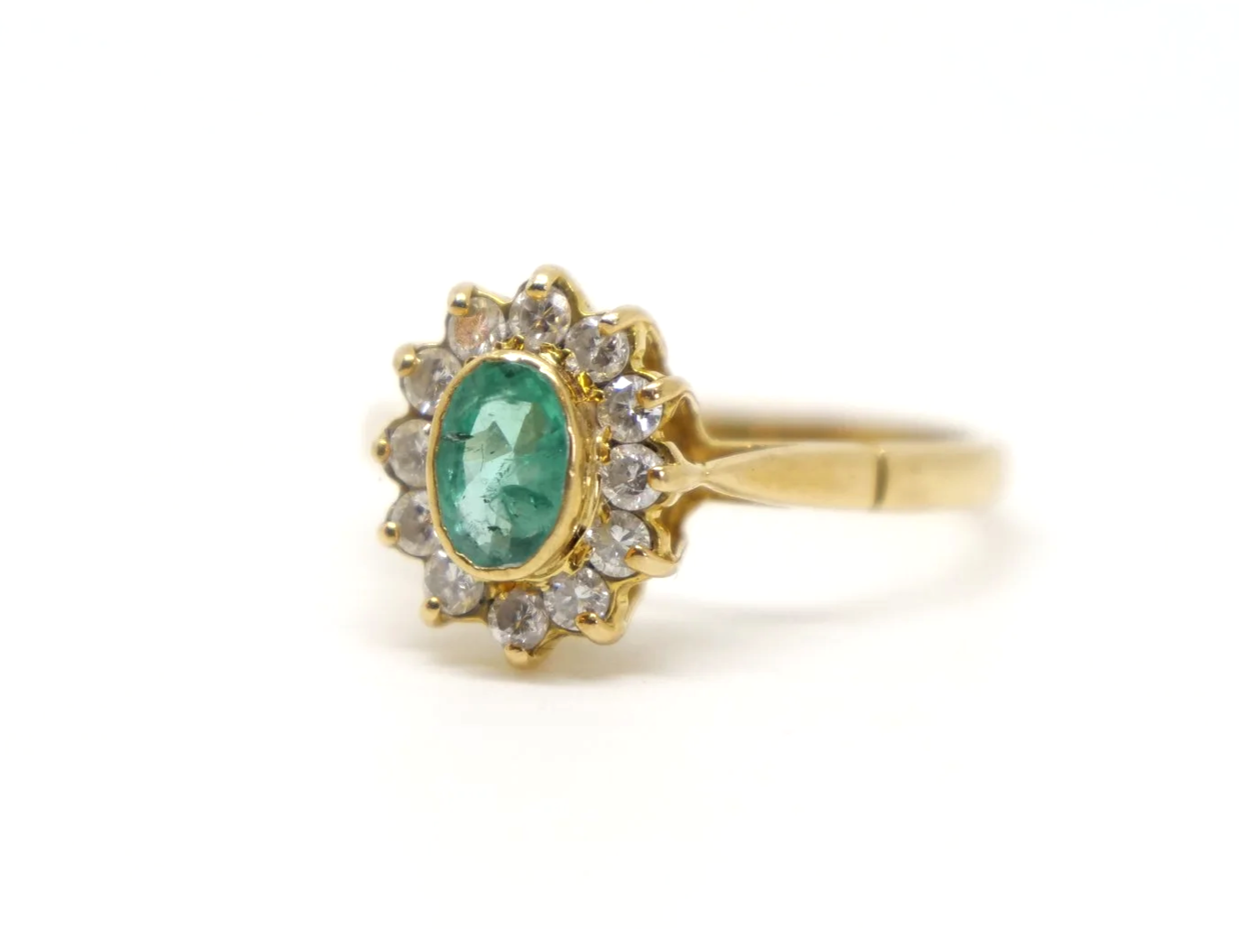 Classic vintage emerald and diamond cluster ring, set with a central oval cut emerald and surrounded by diamonds. All set in 18ct gold.