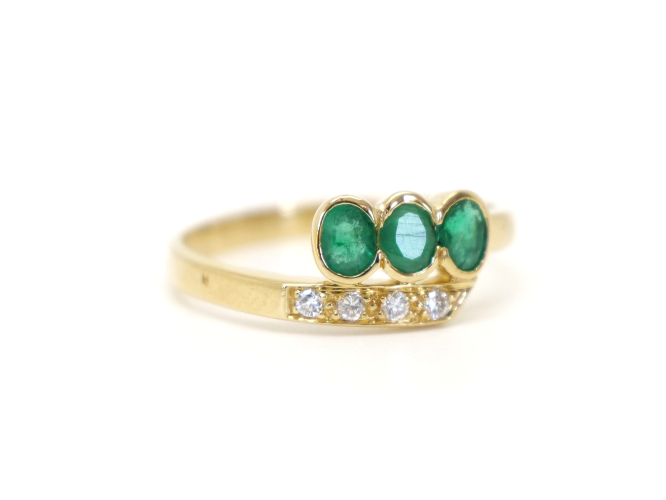 Unusual 18ct gold emerald and diamond twist design ring, set with three oval cut emeralds and four small diamonds.