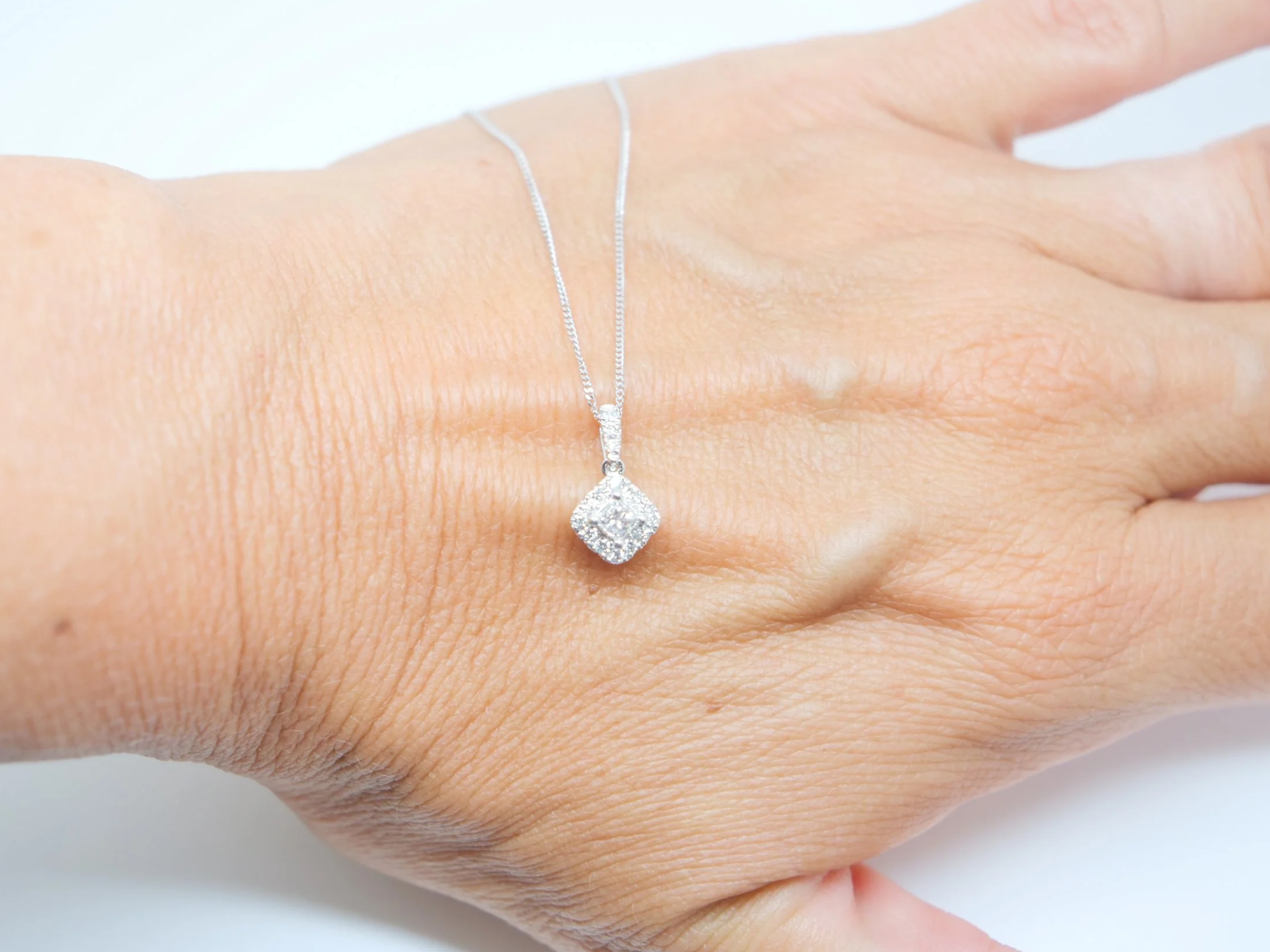 Very pretty 9ct white gold pendant set with a central princess cut diamond, framed by a cluster of brilliant cut diamonds to form a soft diamond shape.