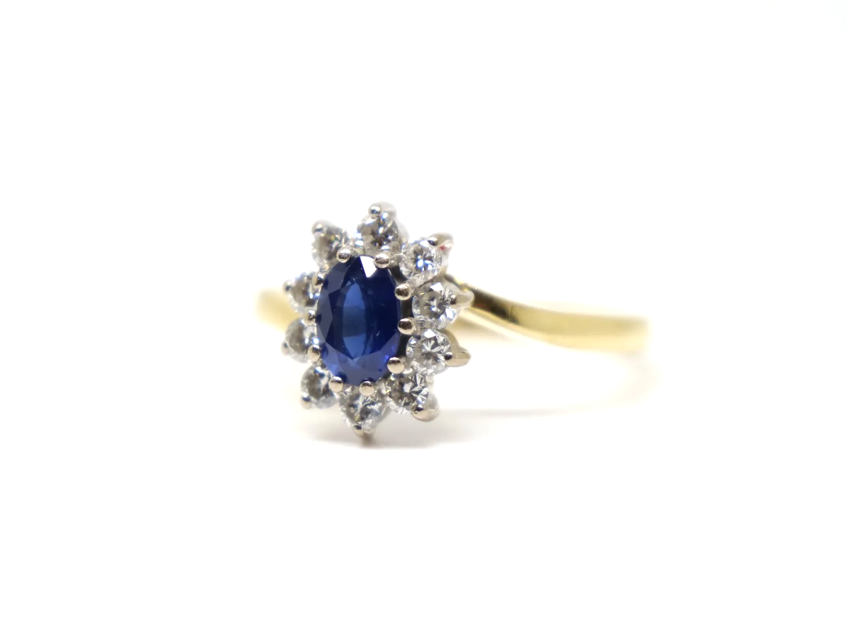 An 18ct gold sapphire and diamond cluster ring from 1998, set with an oval cut sapphire of approximately 0.6 carats at the centre, surrounded by ten round brilliant cut diamonds of 0.4 carats