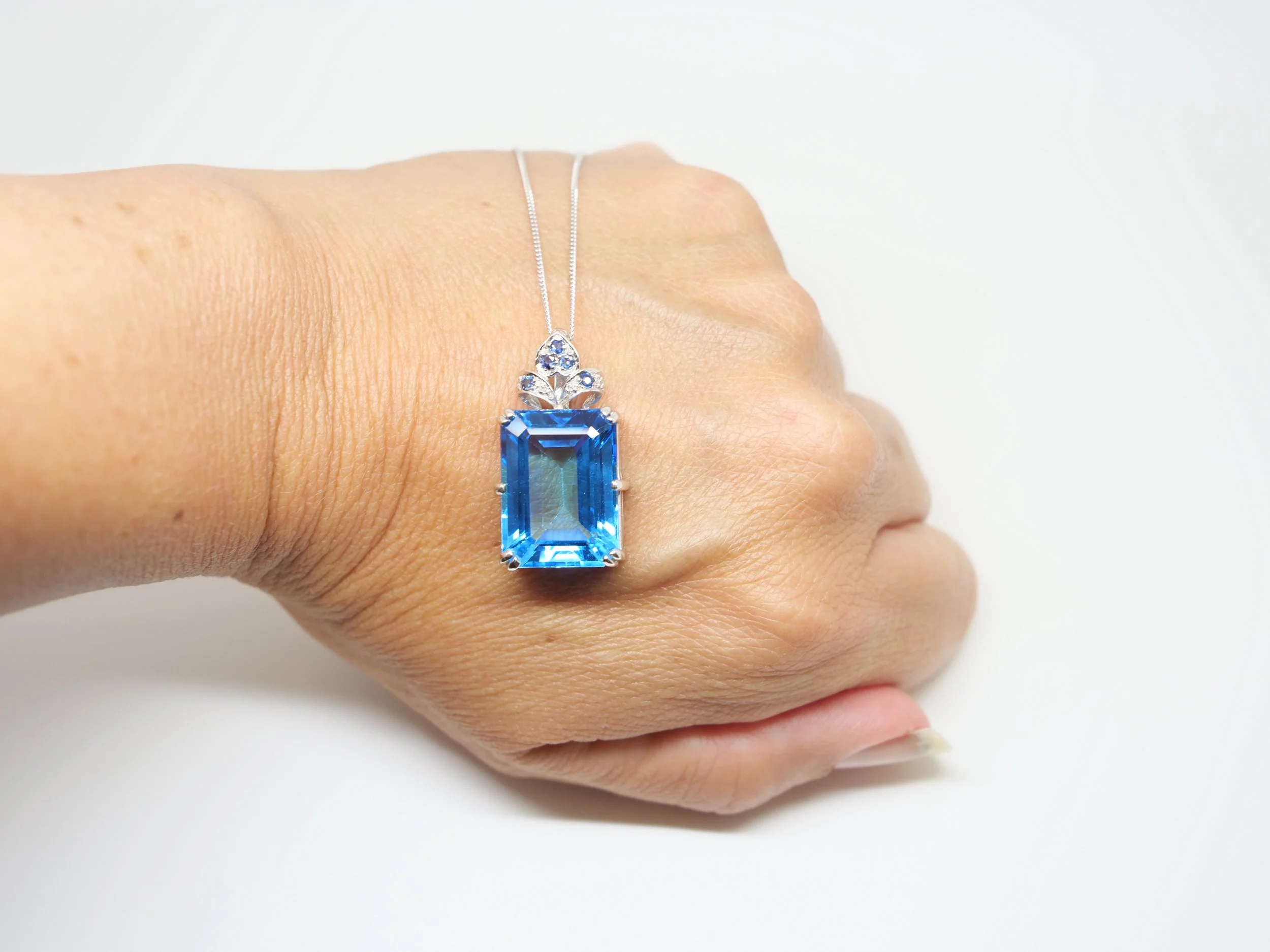 Stunning 9ct gold large blue topaz and sapphire pendant, set with a 26ct emerald cut blue topaz with a sapphire floral design above.