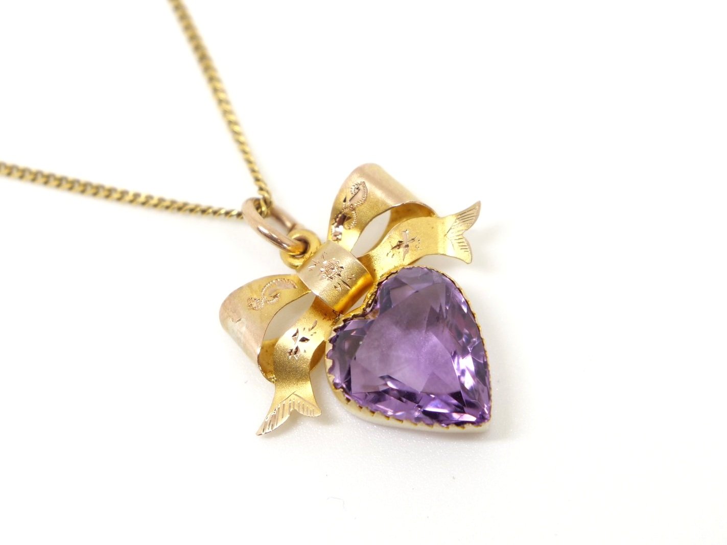 Beautiful 9ct gold turn of the century amethyst pendant, cut into a heart design. Lovely bow with etched designs above the amethyst heart. With (later) 9ct chain.