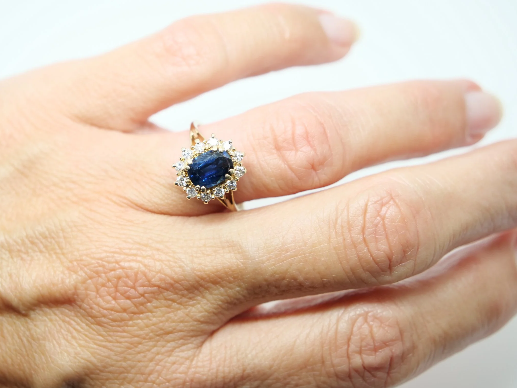 Classic sapphire and diamond cluster ring in 14ct gold, set with an oval cut sapphire of approximately 1.5ct and surrounded by diamonds.
