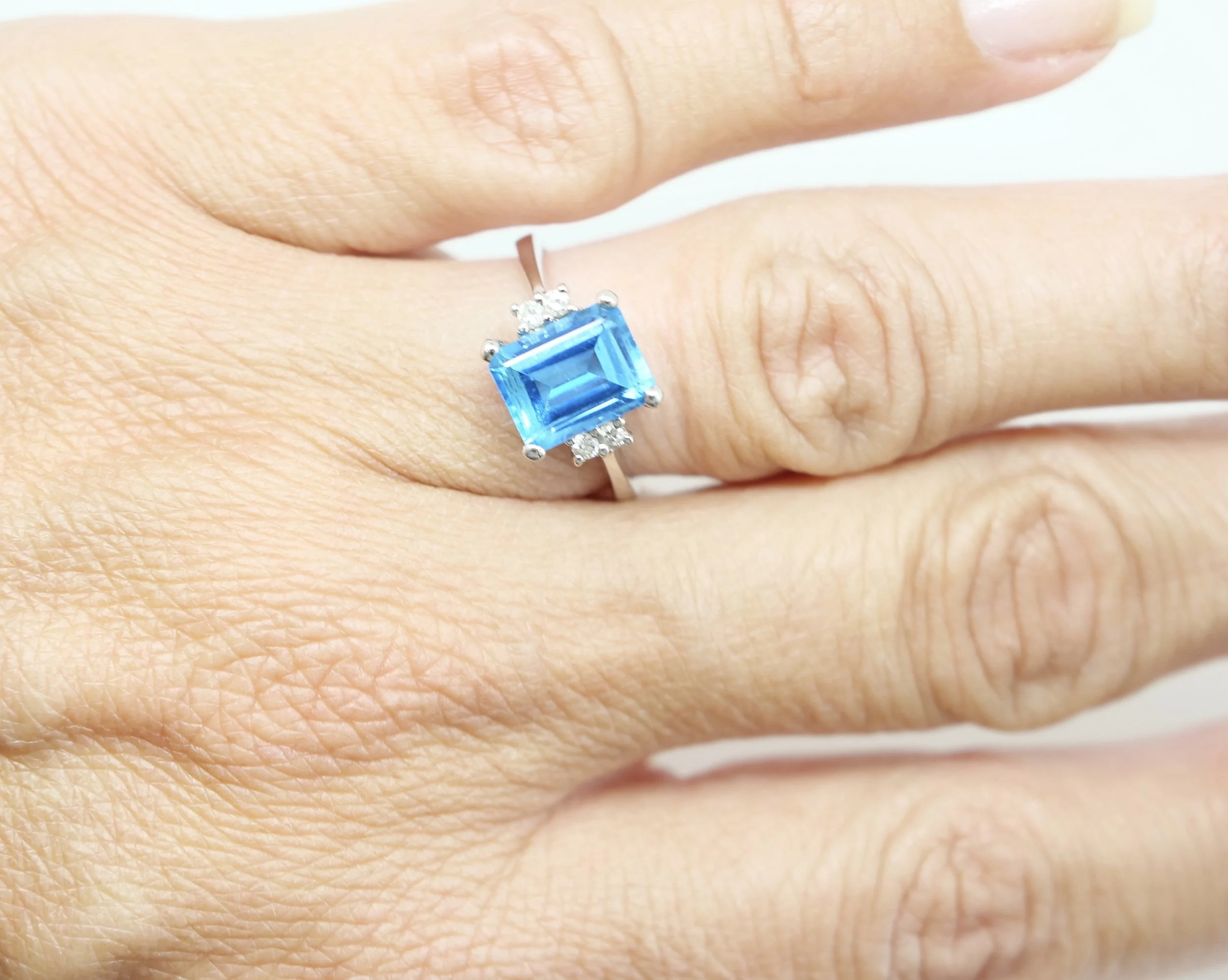 Lovely 18ct gold blue topaz and diamond ring, set with an emerald cut blue topaz of approximately 3.4cts, with two small diamonds to each shoulder.