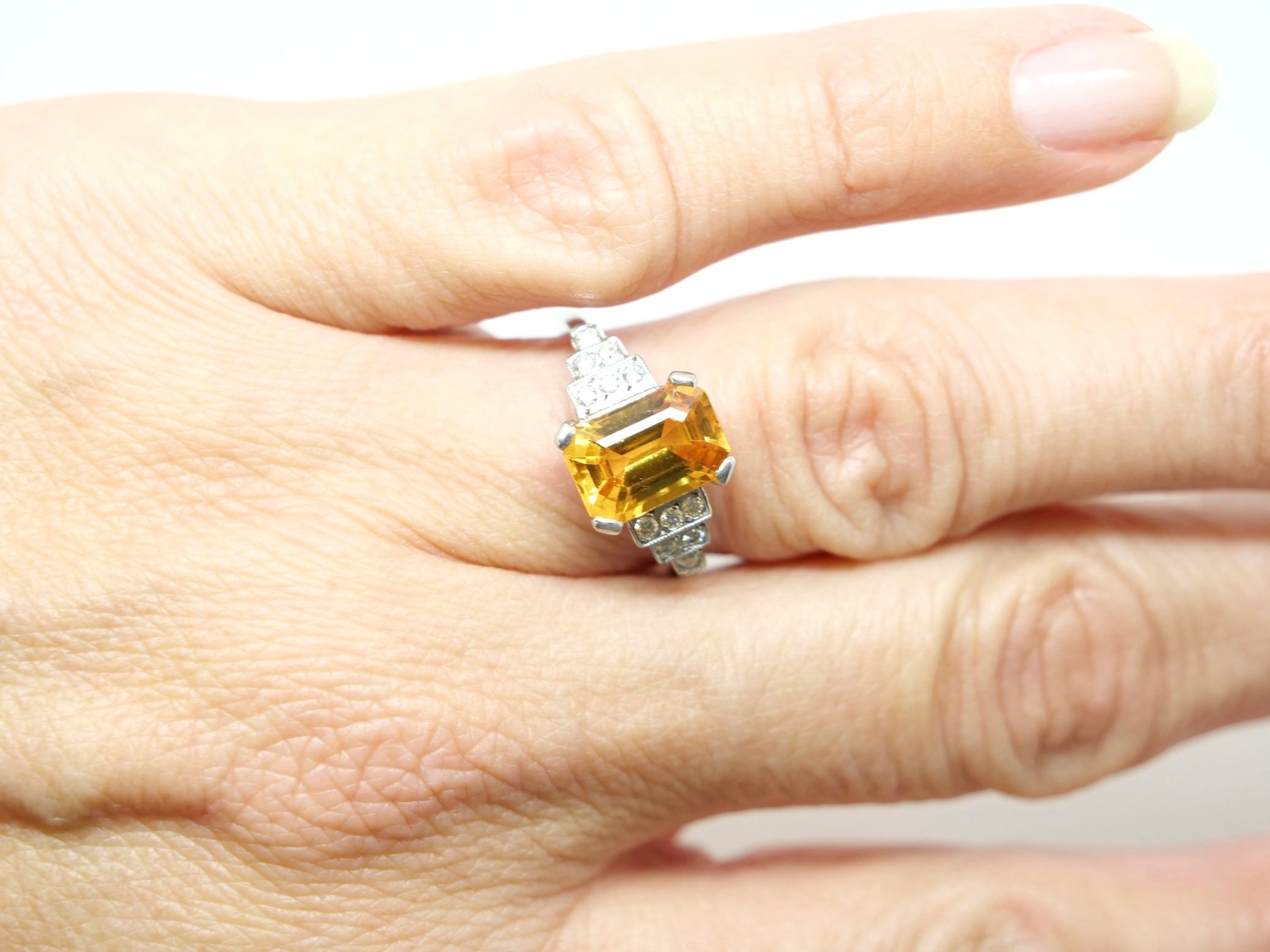 Art Deco style platinum yellow sapphire and diamond ring, set with an emerald cut yellow sapphire of approximately 2.5ct. Diamonds set into step design to each shoulder.