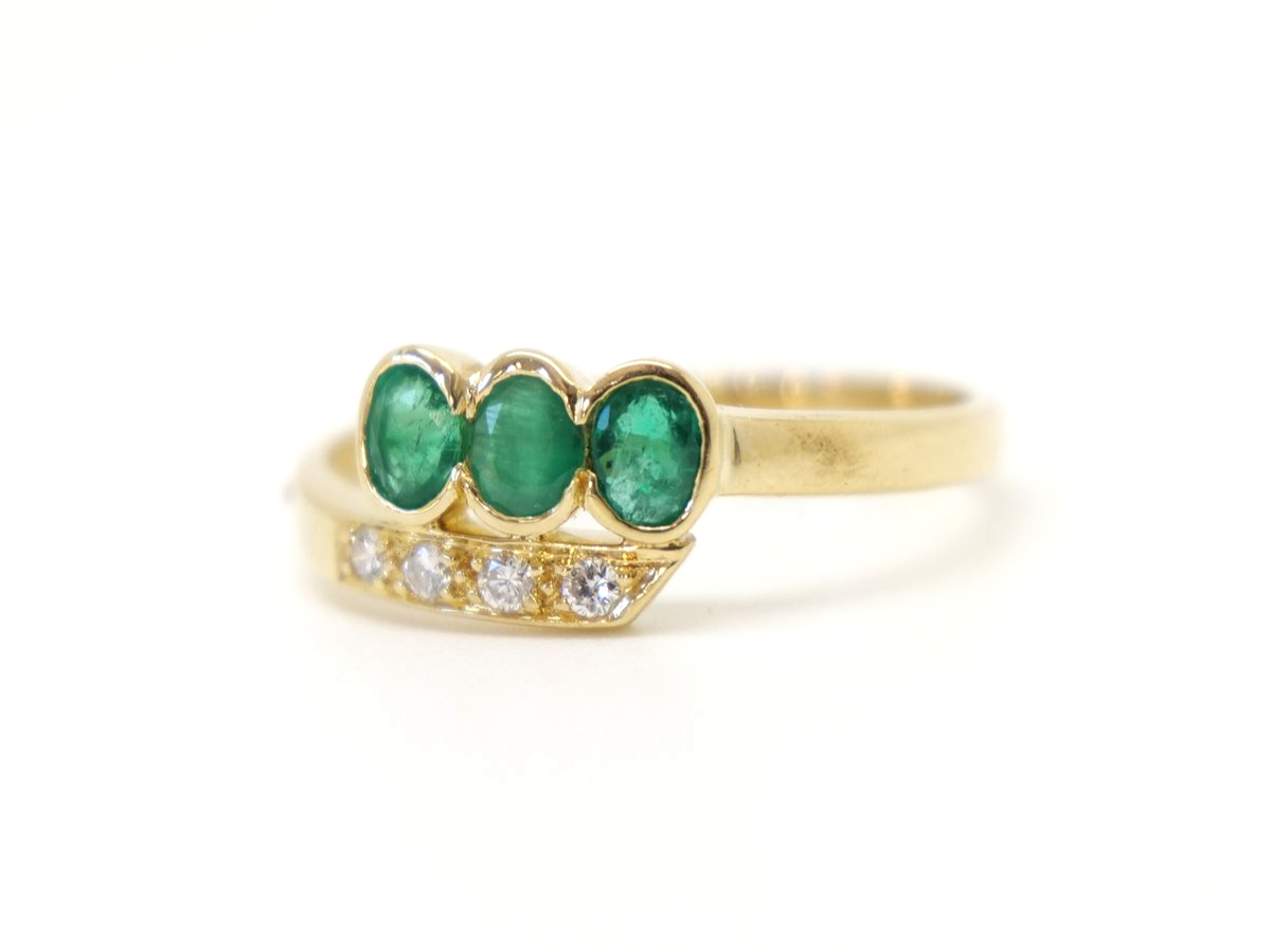 Unusual 18ct gold emerald and diamond twist design ring, set with three oval cut emeralds and four small diamonds.