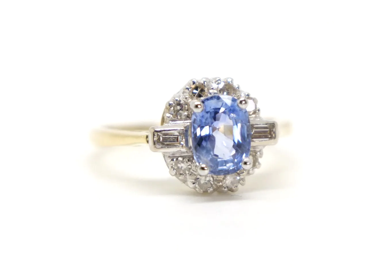 Stunning 18ct gold sapphire and diamond ring, set with an oval light blue sapphire and surrounded by diamonds, with a baguette diamond to each shoulder.