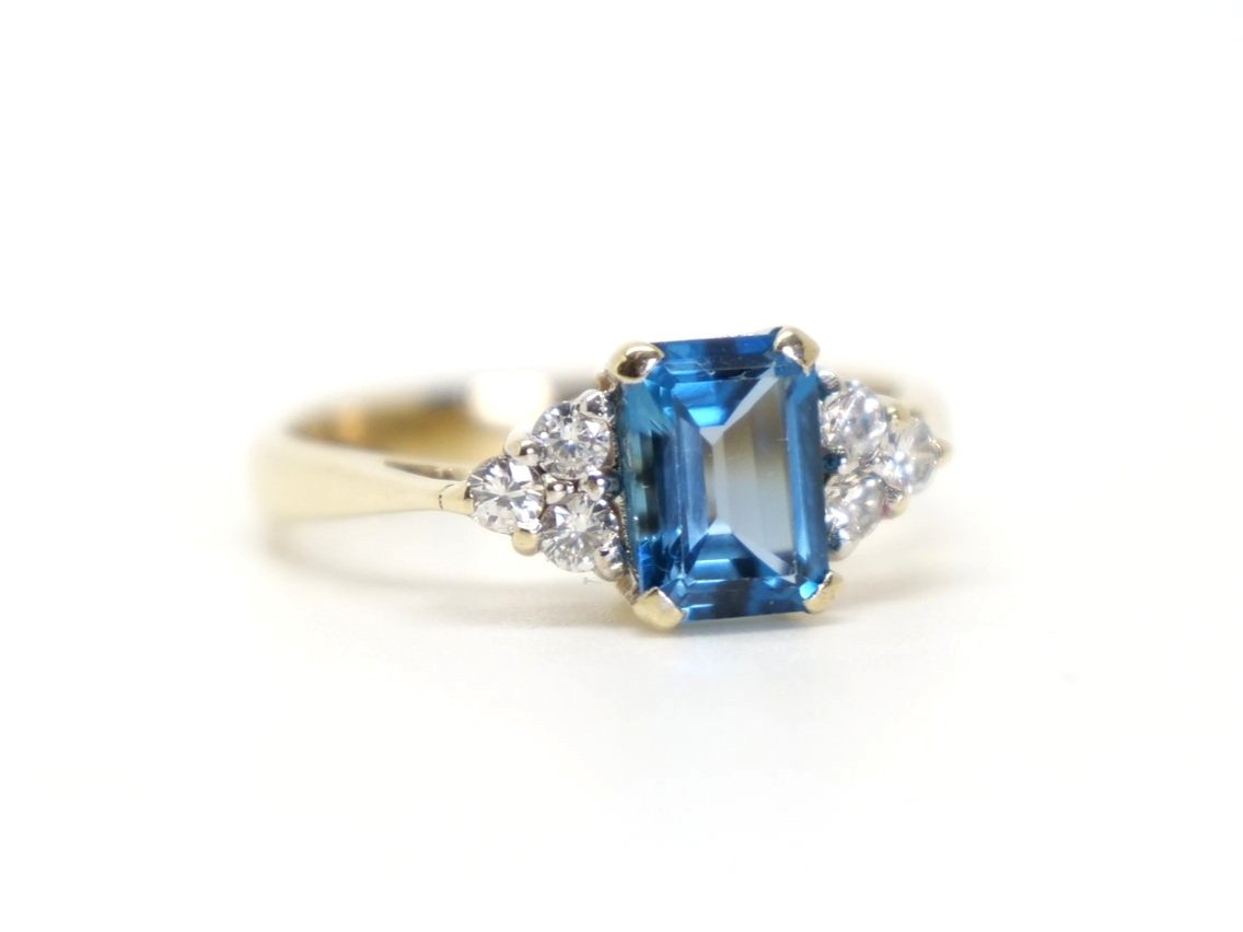 Very pretty 9ct gold blue topaz and diamond ring, set with an emerald cut blue topaz, with three diamonds to each side.