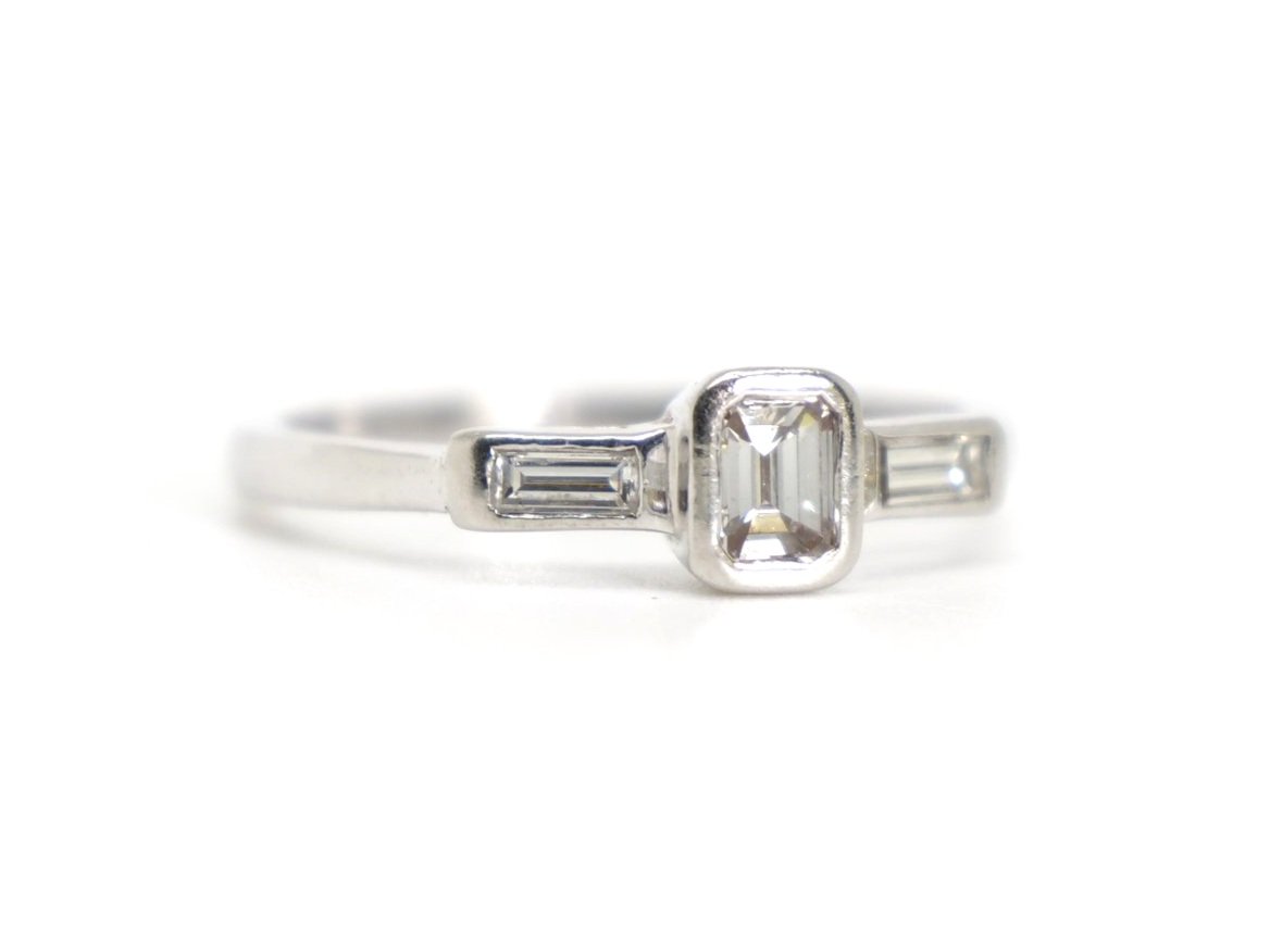 Unusual platinum diamond ring, set with a central emerald cut diamond, with a baguette cut diamond to each shoulder. Total diamond weight 0.5ct.