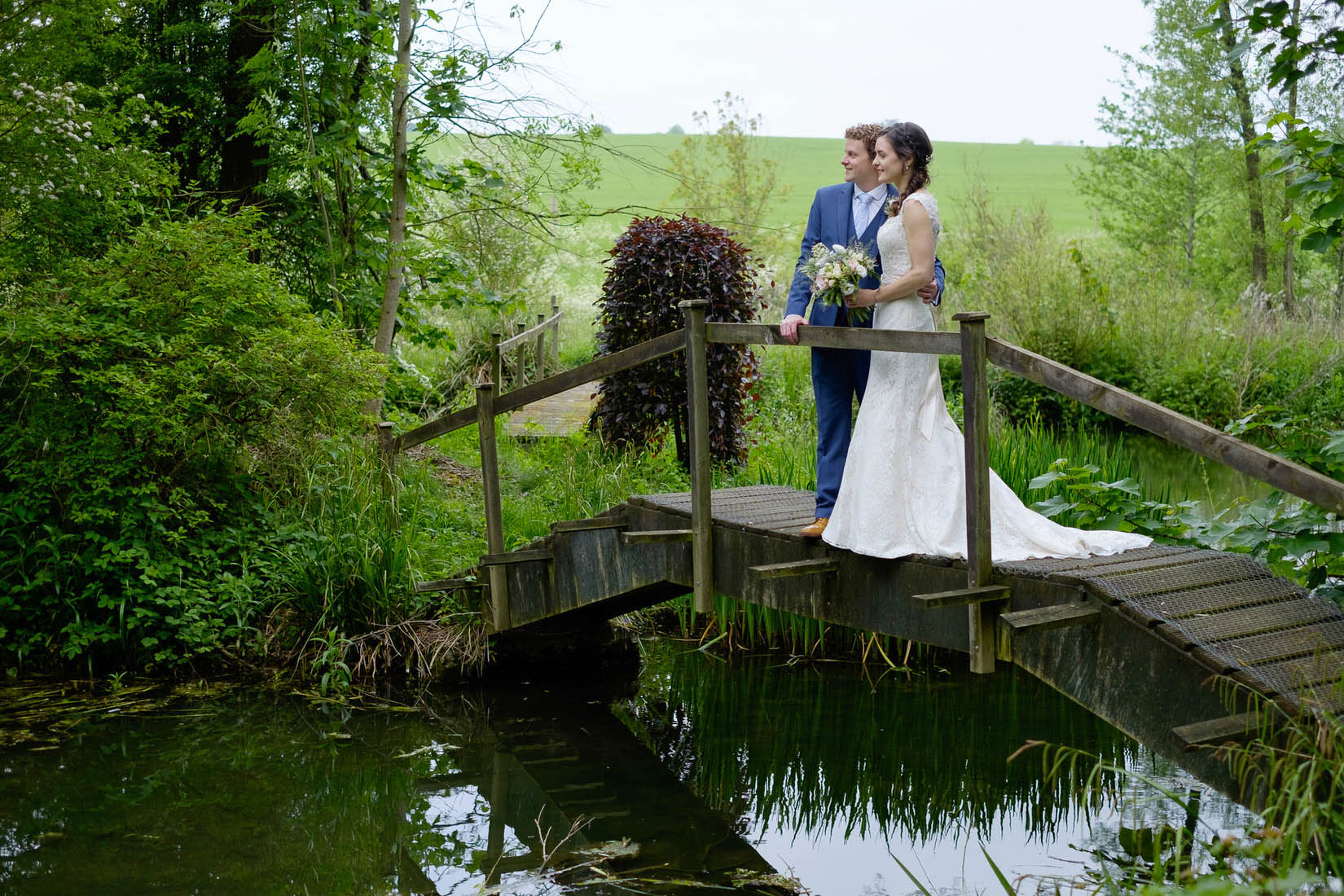 A bride and groom on a bridge over a lake at Great Barn Wedding Venue, Aynho. Photo by Sam and Steve Photography