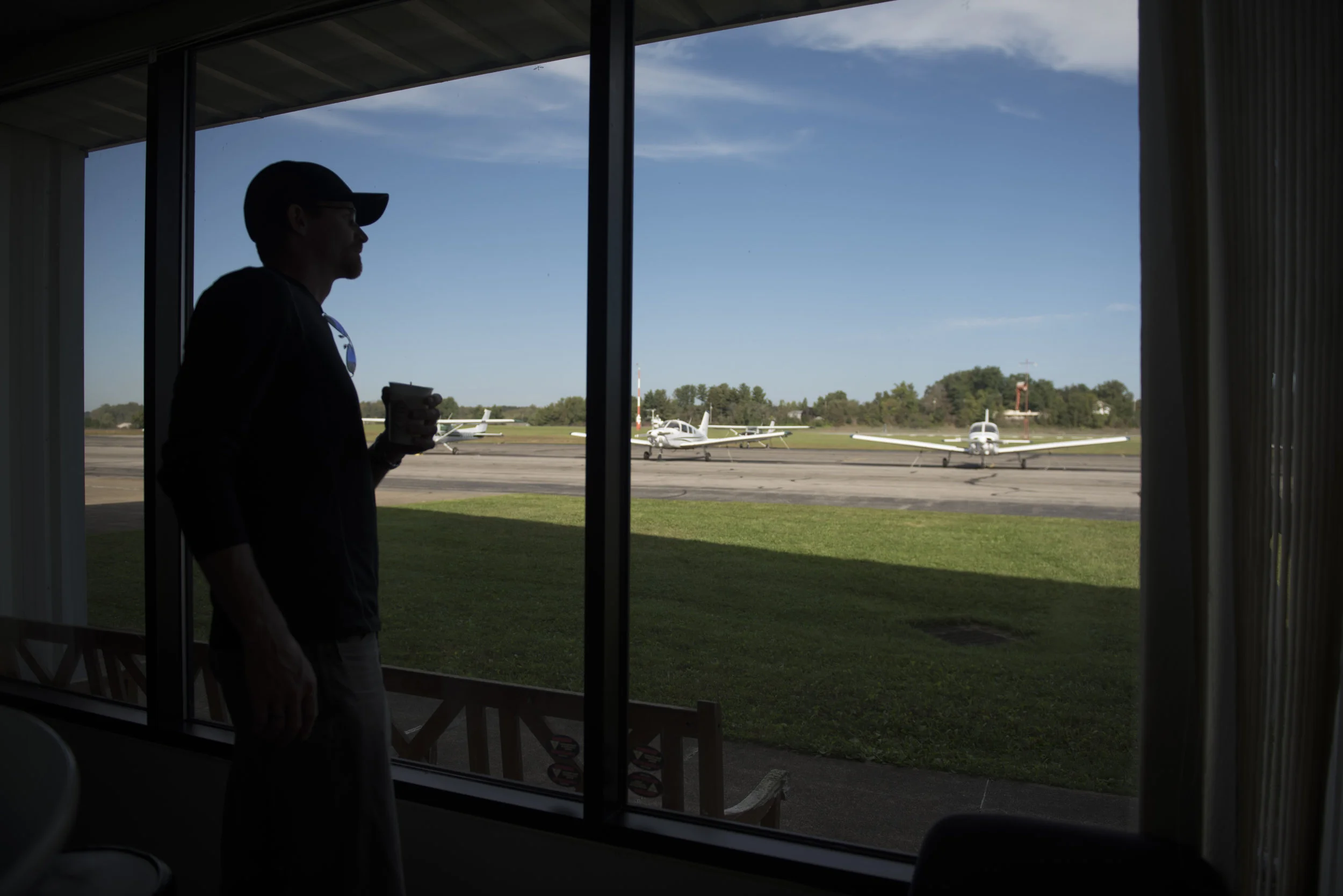 Flight instructor Eric Lee watches planes take off through the window of the training center at Gordon K. Bush airport on Sept. 24, 2017.